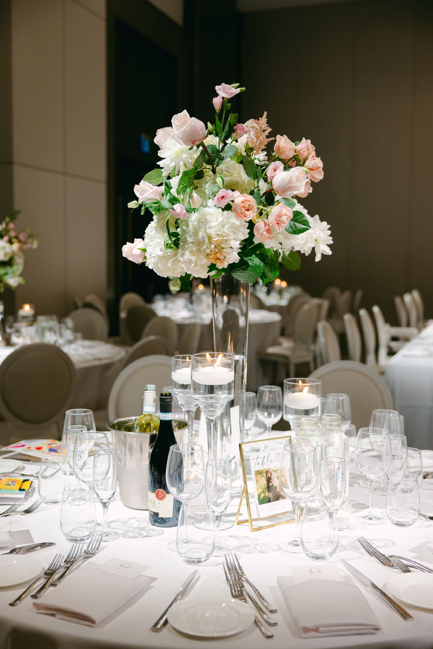 Romantic table setting with tall pink and white floral centerpiece and crystal glassware.