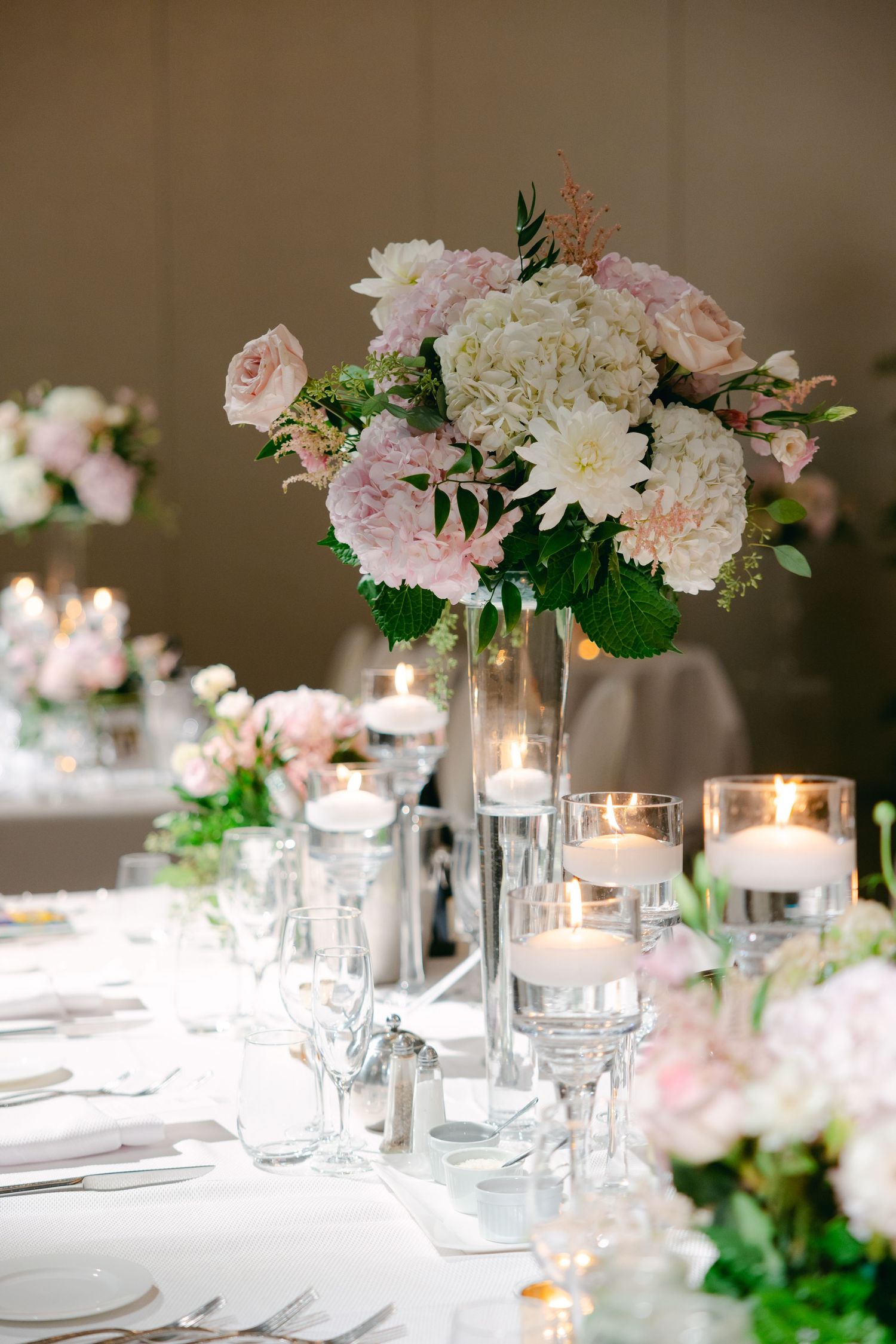 Luxurious pink and white floral centerpiece with candlelight for wedding reception table.