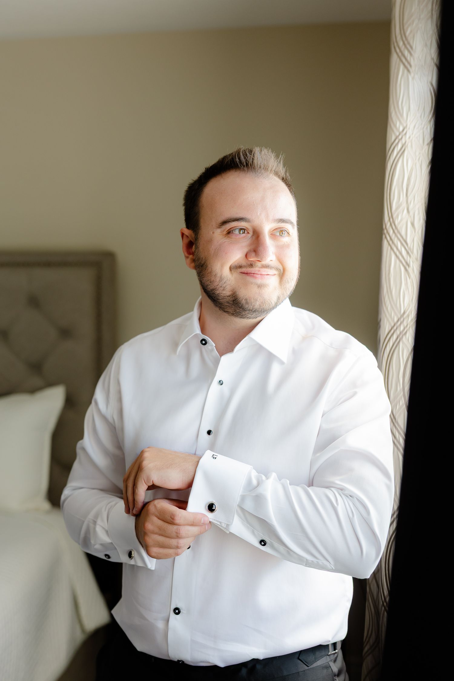 A person wearing a formal white dress shirt with black buttons smiles warmly.