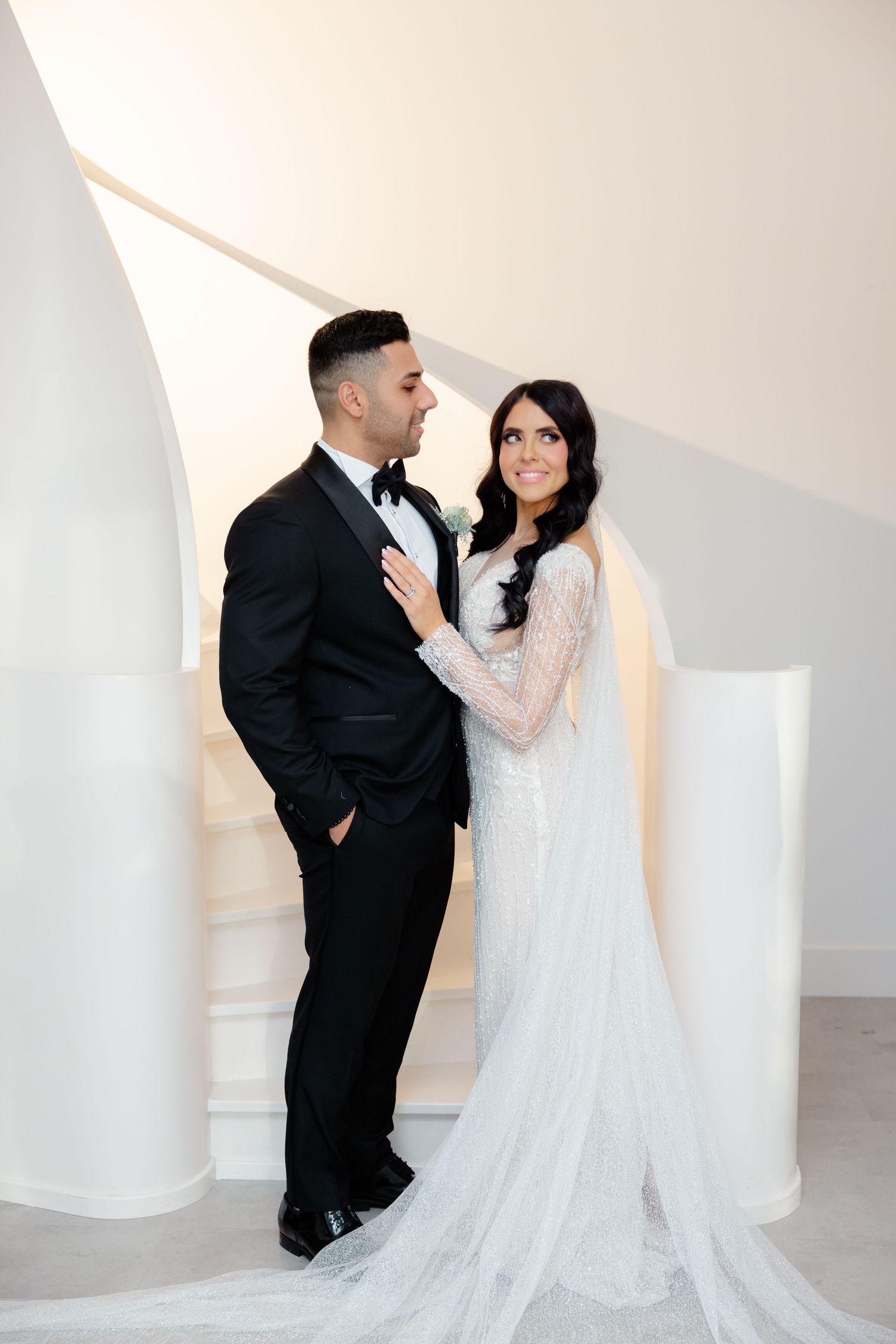 Modern architectural wedding photo with couple posed on white spiral staircase.
