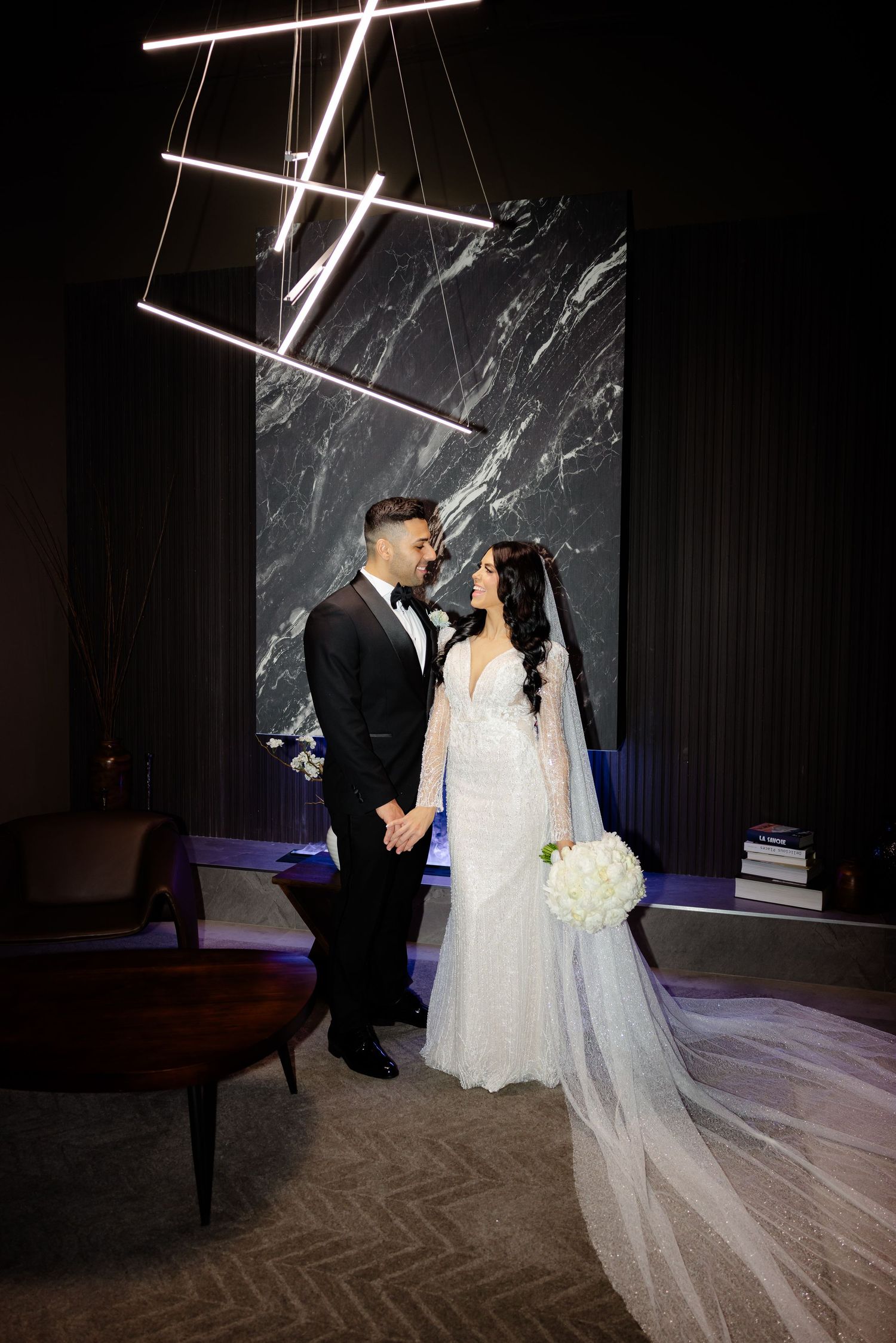 Modern wedding portrait with geometric light installation and dramatic marble wall backdrop.