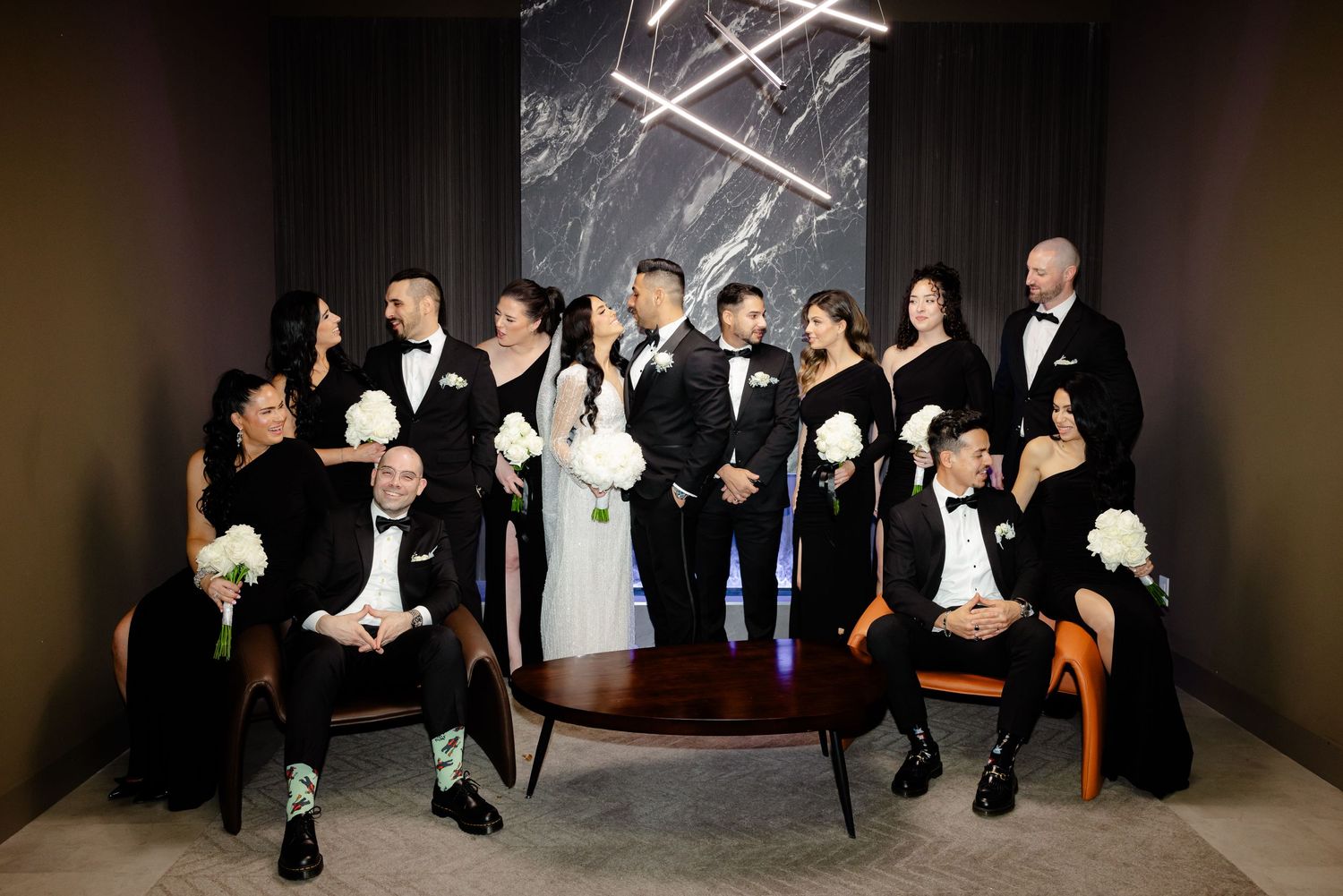 Elegant wedding group portrait with bridesmaids and groomsmen in stylish black formal wear.