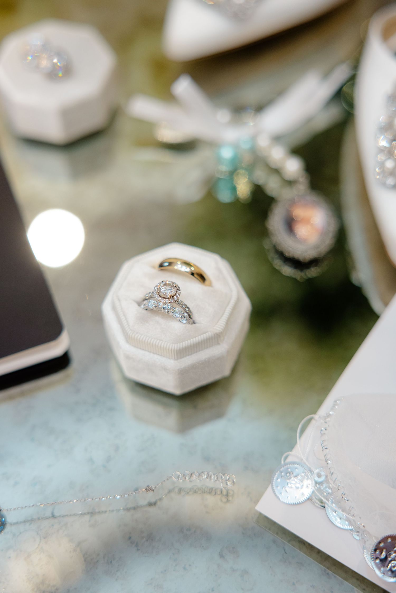 Wedding rings displayed in elegant white hexagonal box with other jewelry pieces on reflective surface.