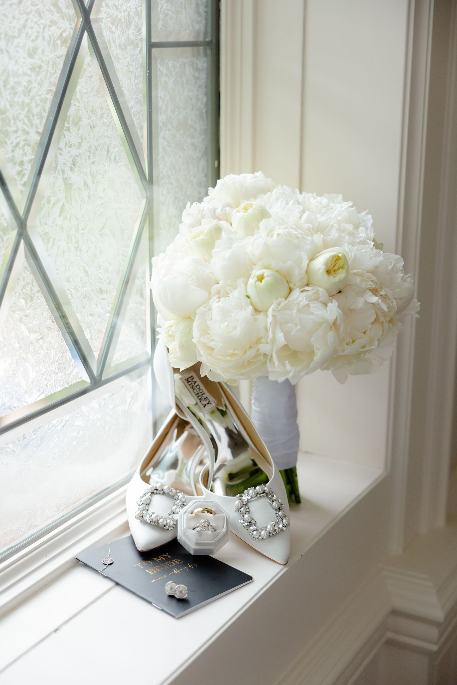 Bridal bouquet of white peonies next to elegant heels on a window ledge.