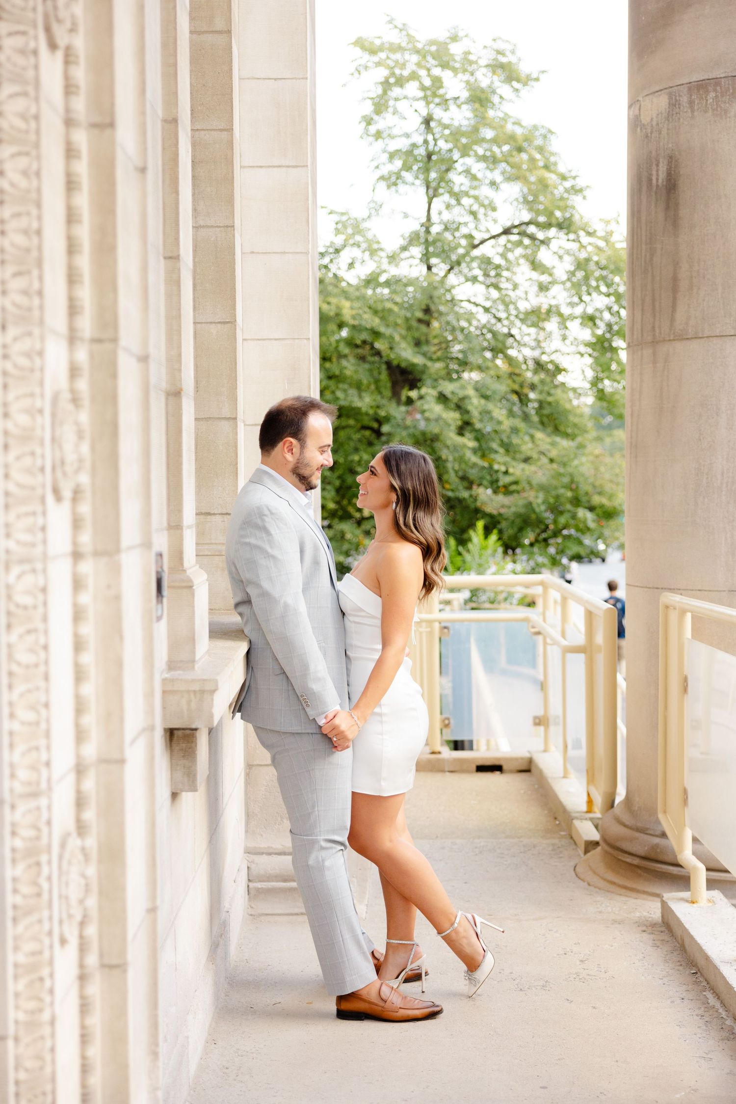 A couple stands close together on an elegant outdoor terrace with classical architecture.