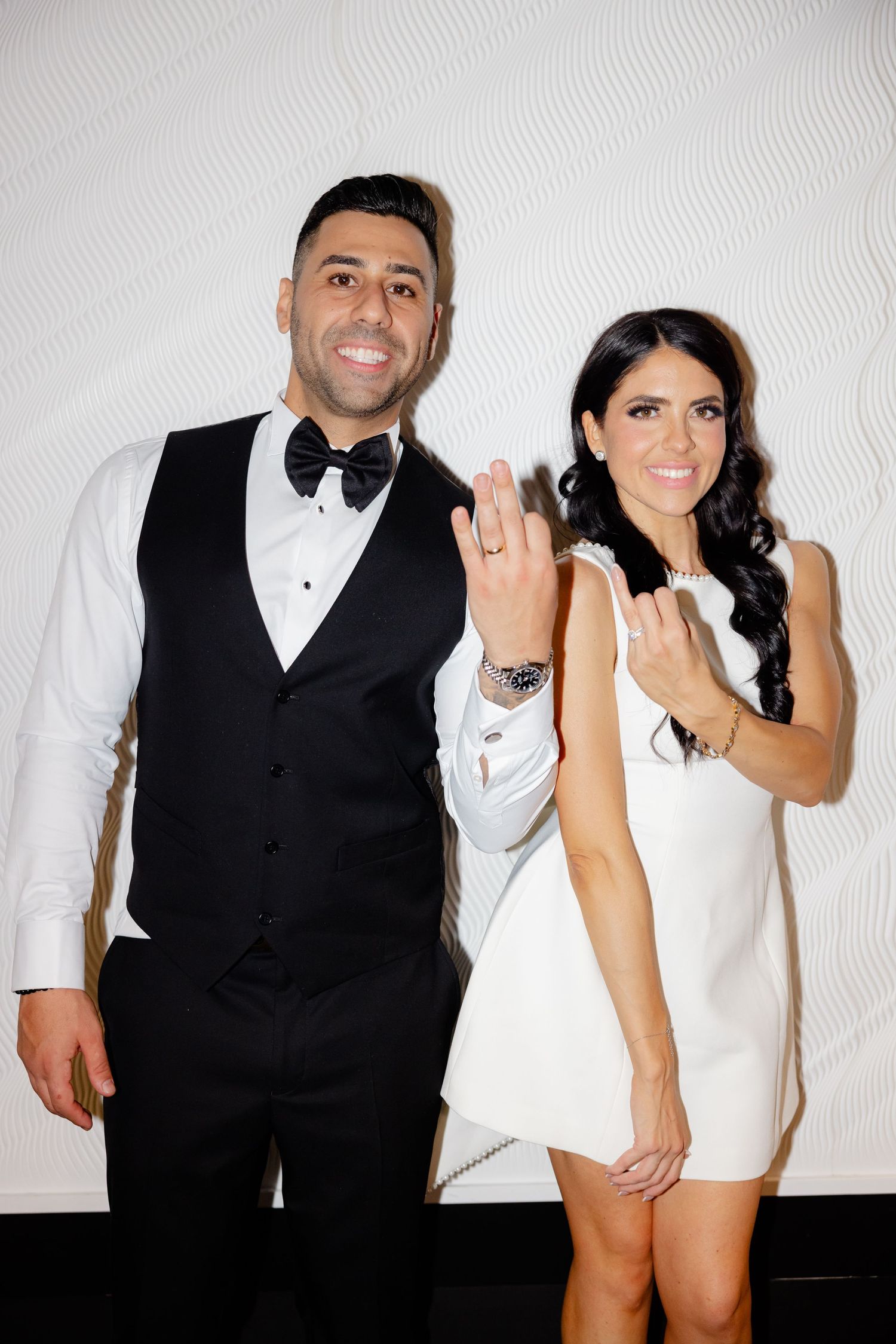 Newlyweds show off rings in formal black and white attire.