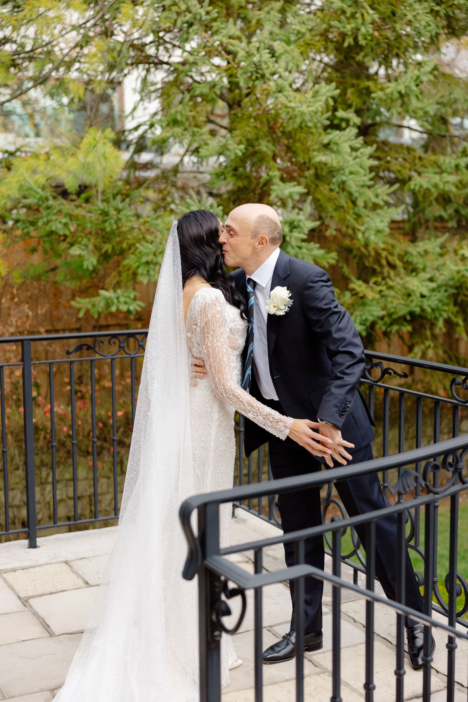 A romantic wedding moment with a bride in lace and groom in navy sharing a kiss on an outdoor stone terrace.