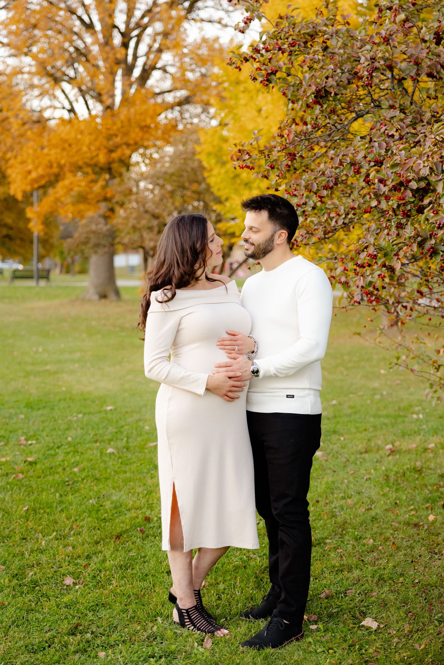 A couple embraces in a park during autumn, surrounded by trees with golden foliage.