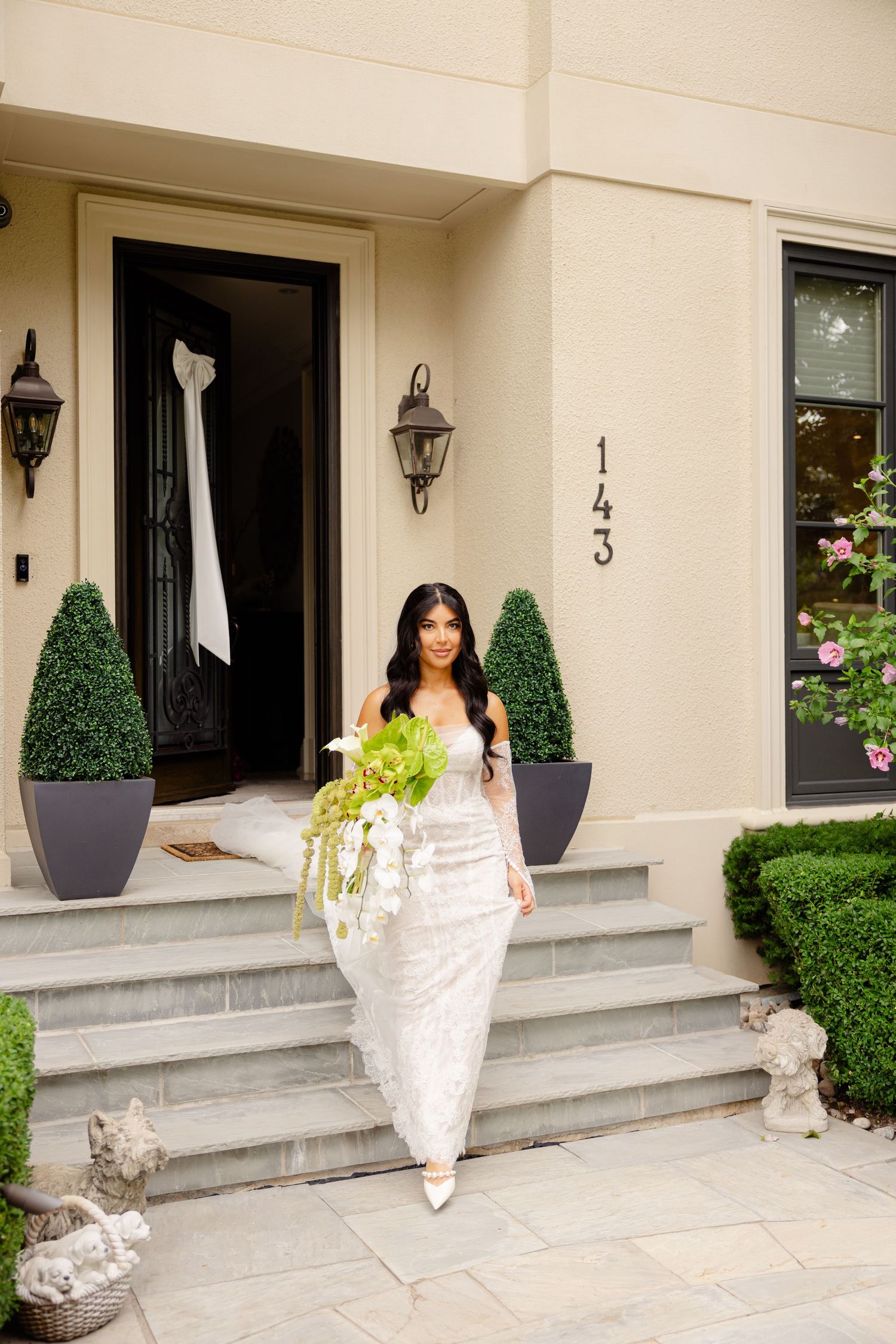 Elegant cream-colored building exterior with manicured topiaries and stone steps leading to black front doors.