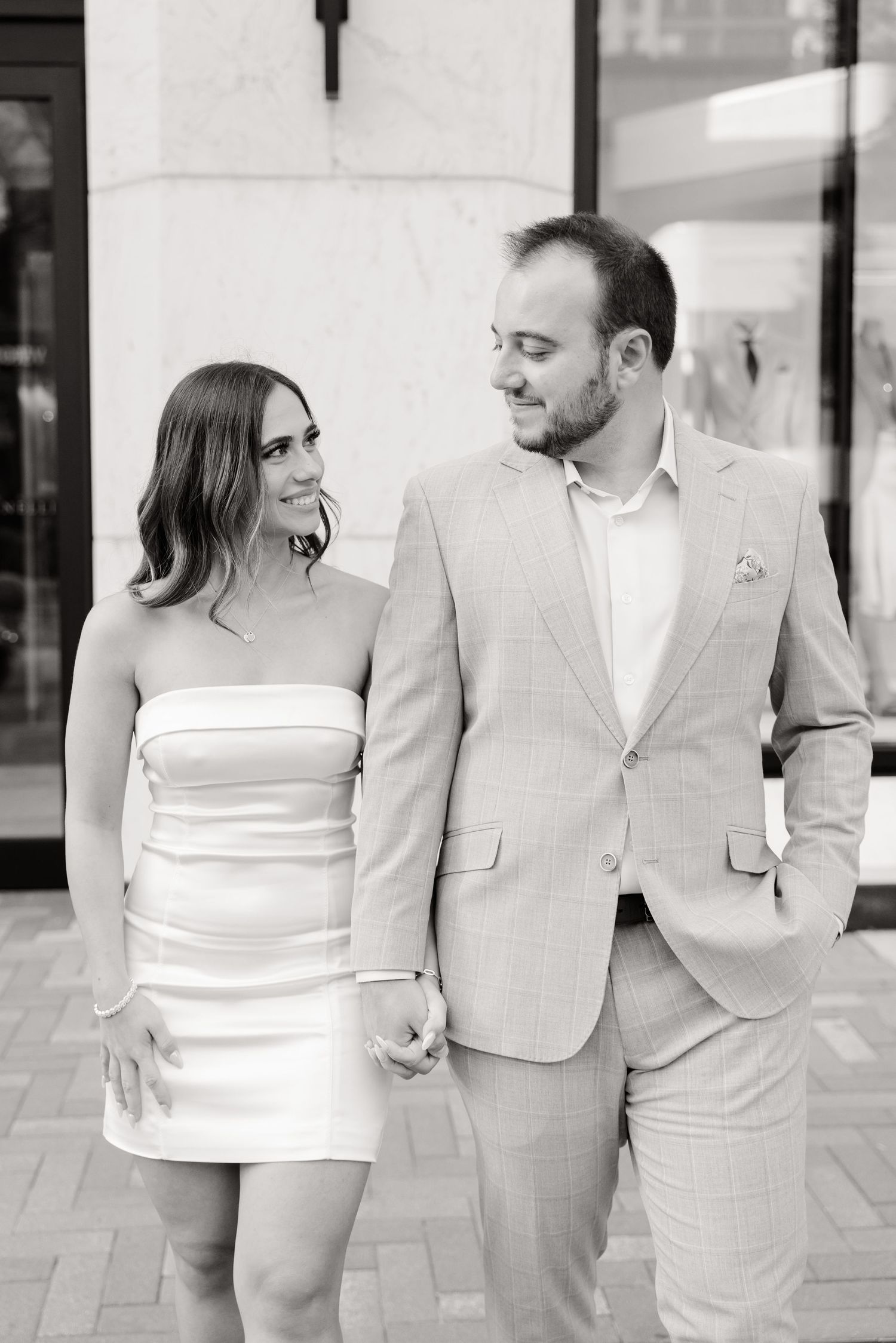 Black and white candid moment of couple sharing a laugh against urban backdrop.