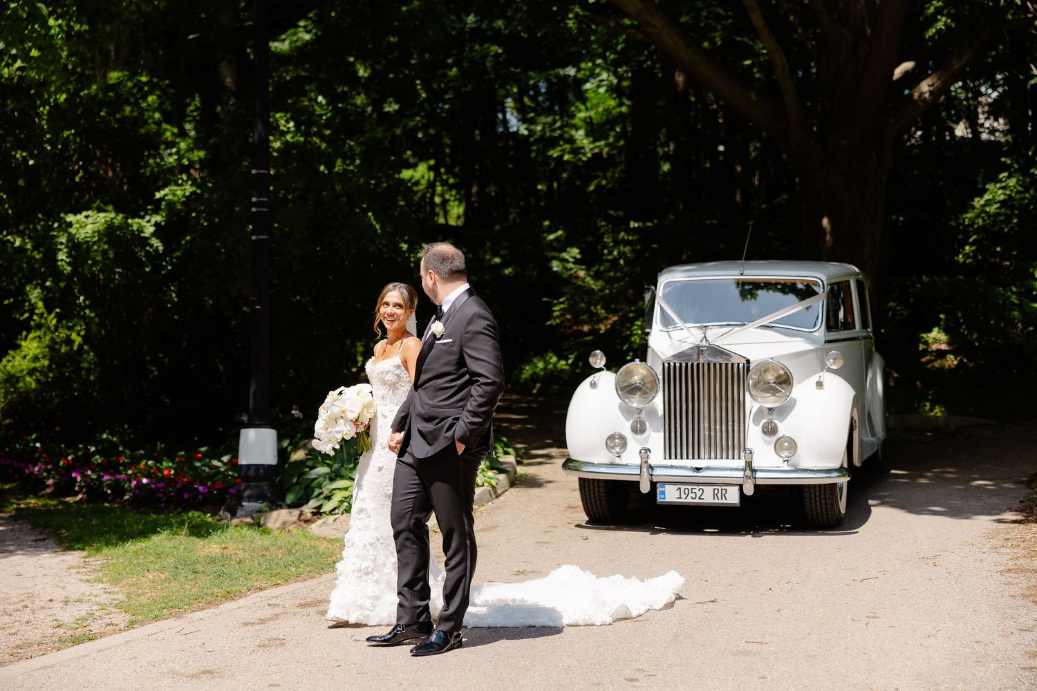 Elegant vintage Rolls Royce parked on a tree-lined driveway during a sunny summer wedding celebration.