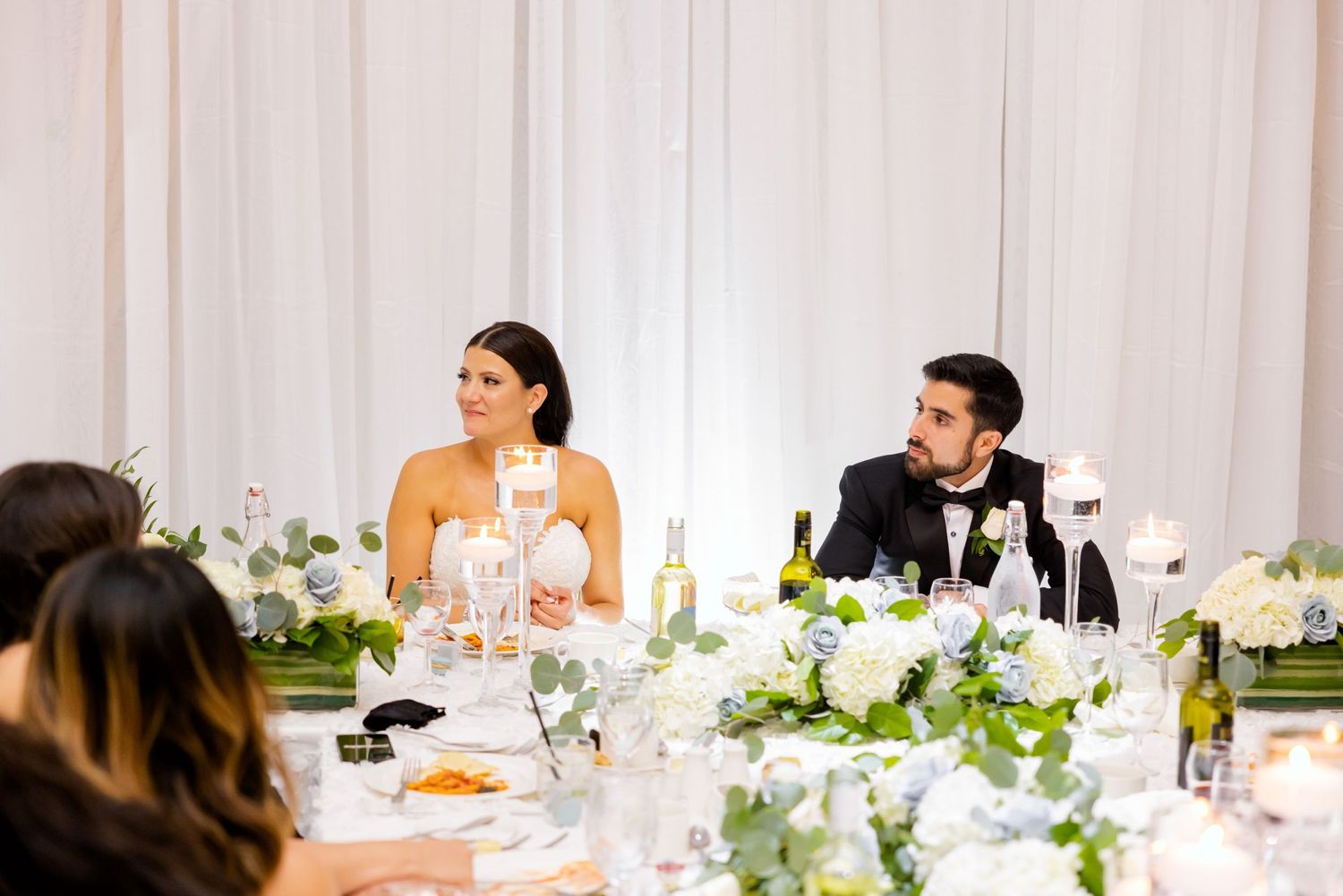 Elegant wedding reception table setup with white floral centerpieces and formal place settings.