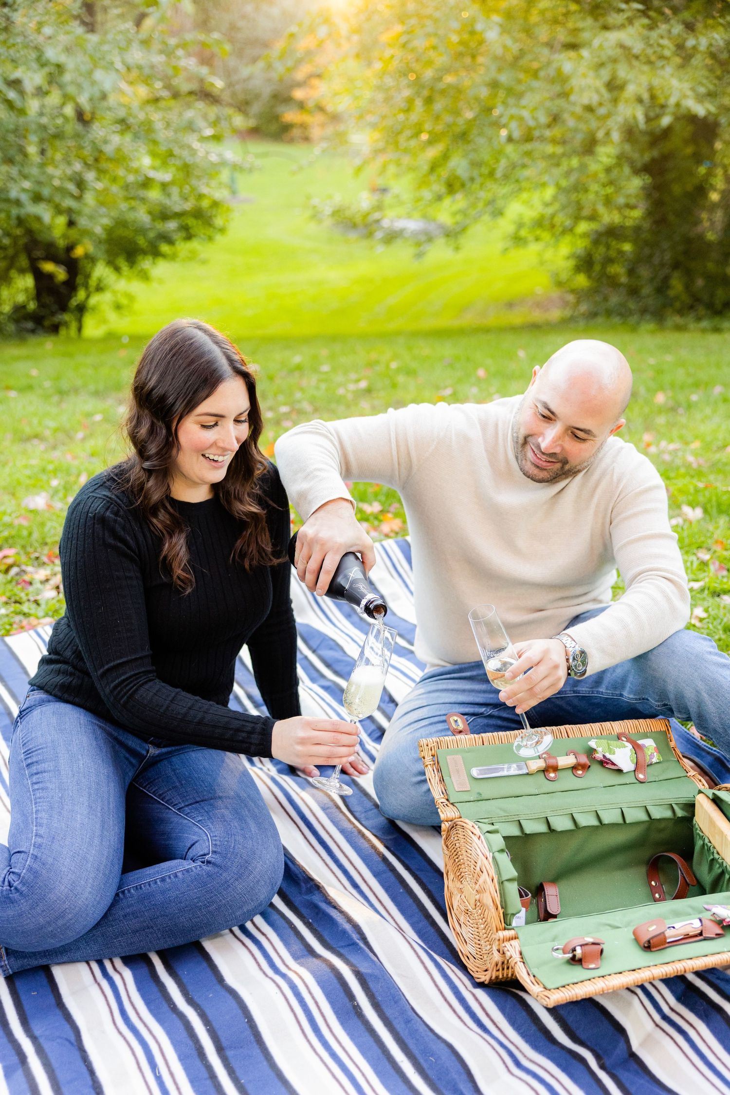 Couple playing tabletop game on striped blanket during sunny outdoor picnic.