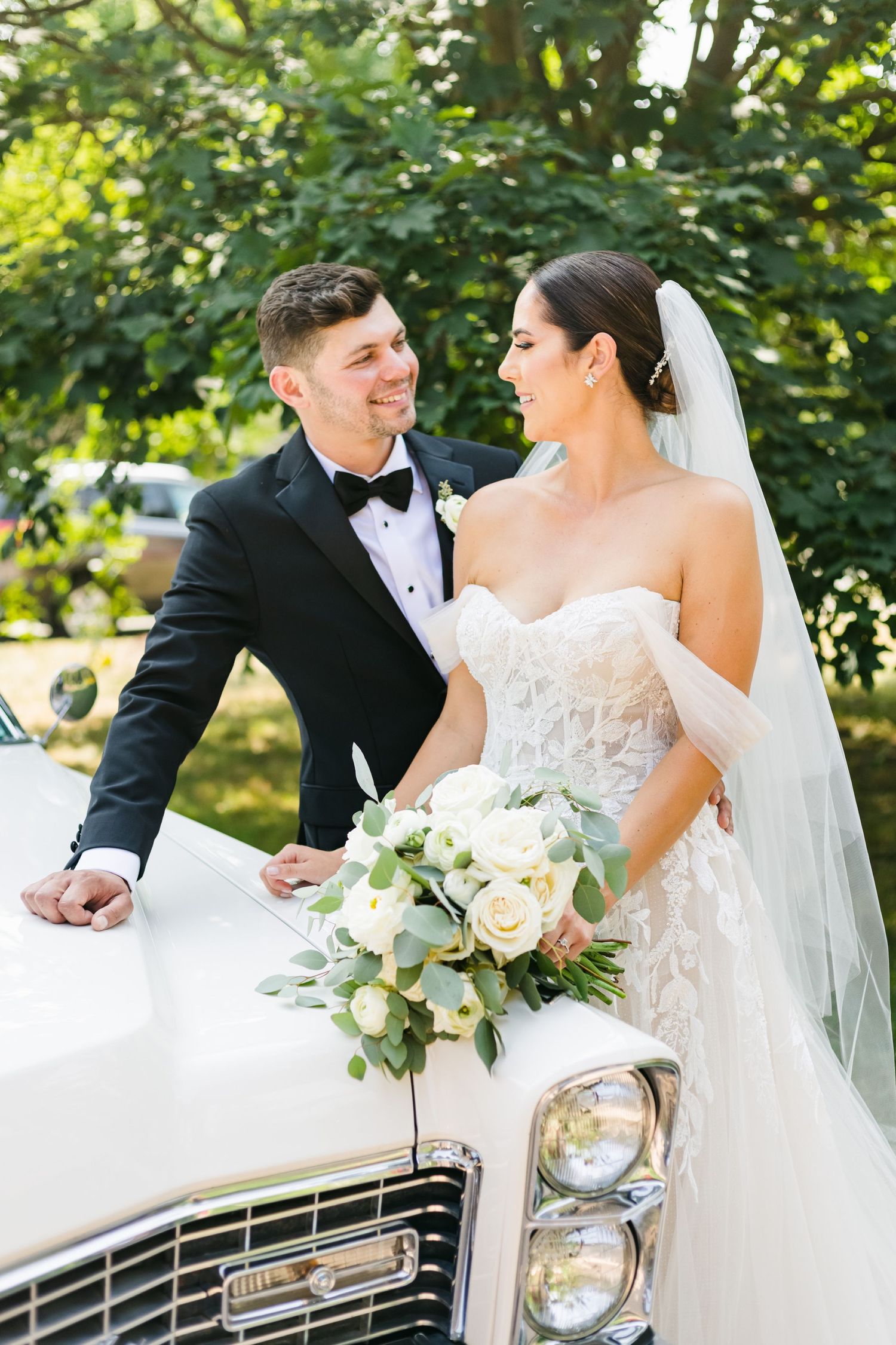 Elegant wedding couple shares joyful moment beside classic white Cadillac.