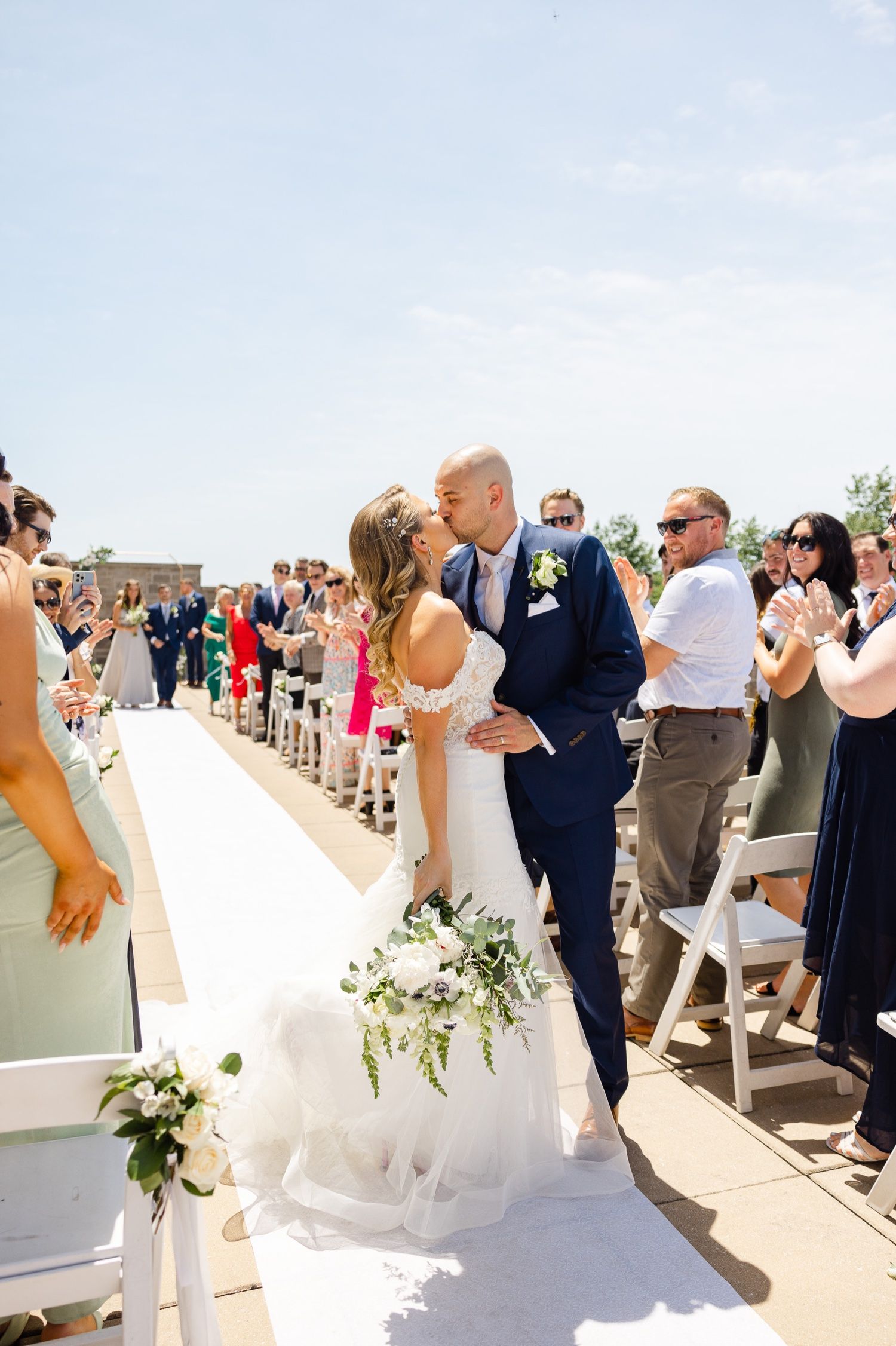 Romantic moment captured during outdoor wedding ceremony with white aisle runner and seated guests.