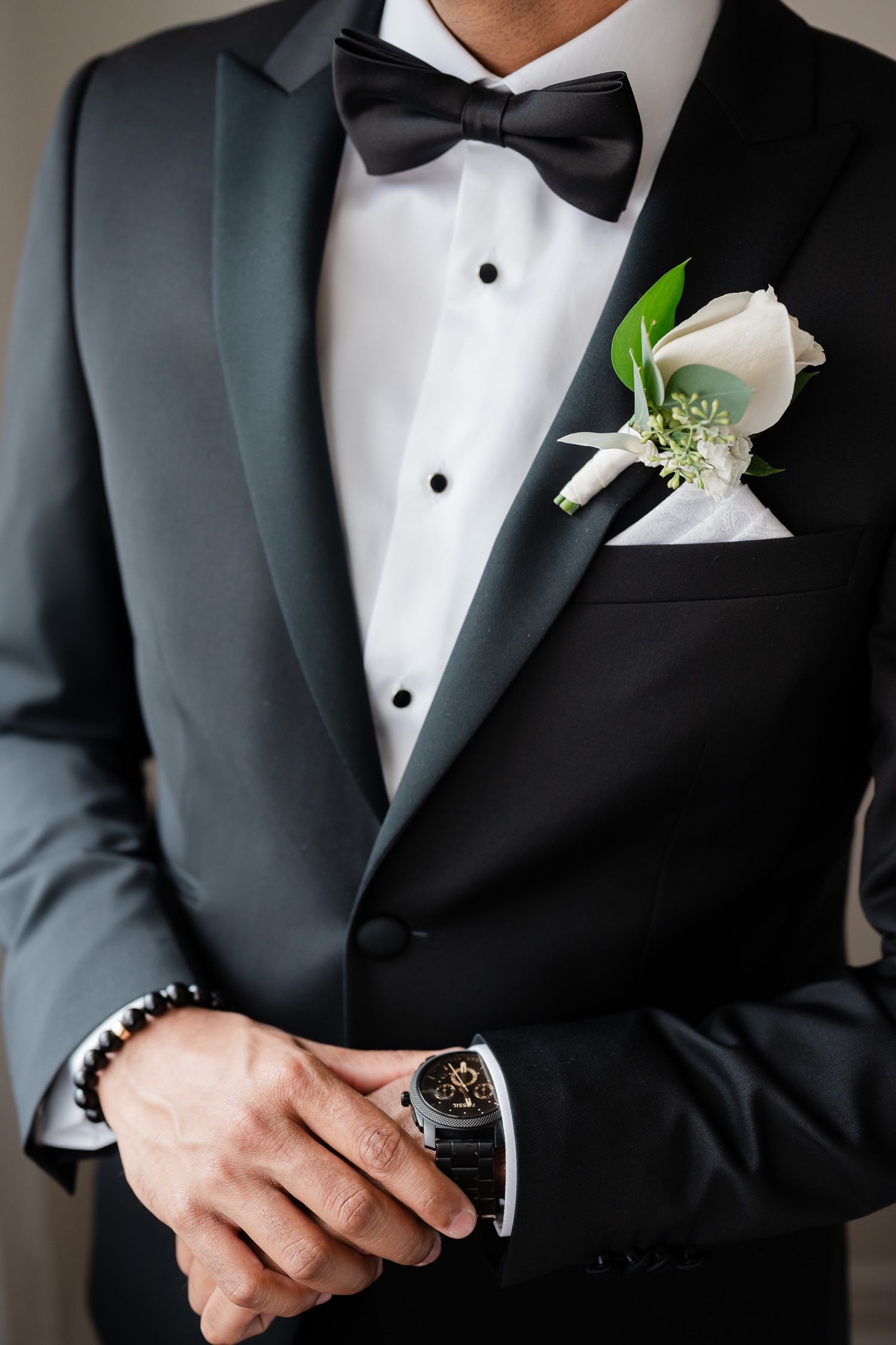 Close-up of black tuxedo with white rose boutonniere and bow tie showing elegant wedding details.