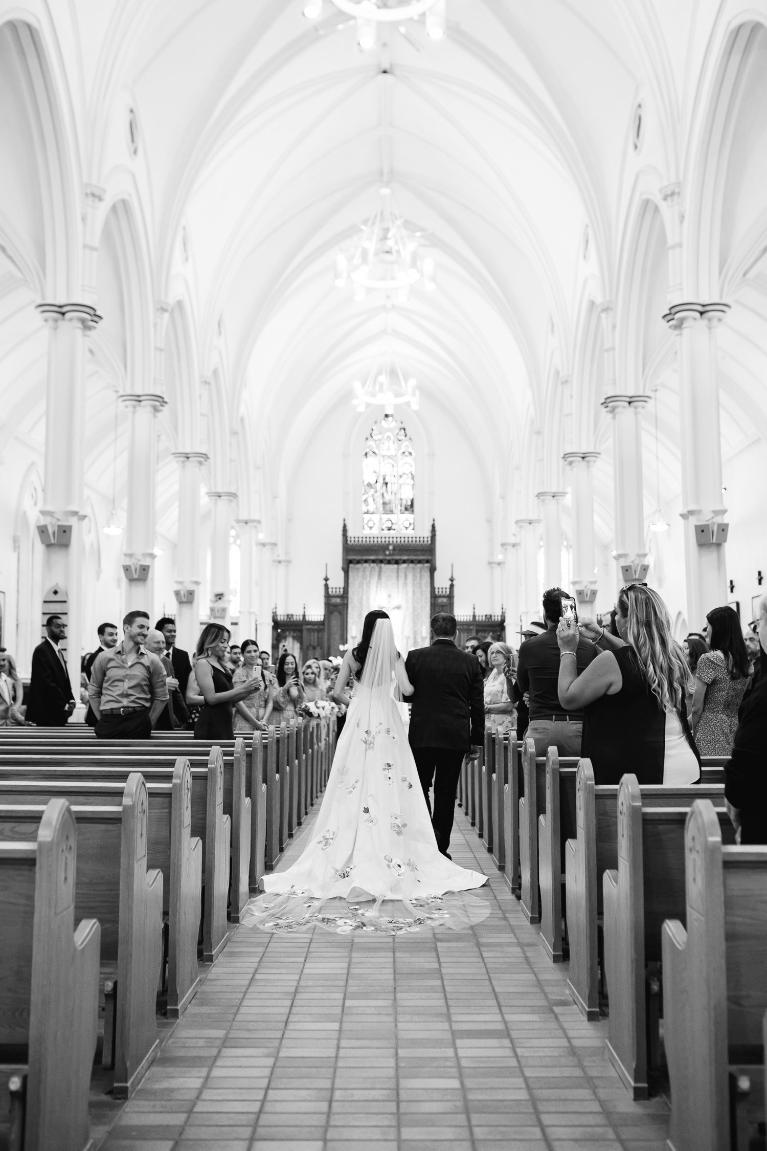 A black and white photo of a wedding ceremony in a grand cathedral with vaulted ceilings and wooden pews.