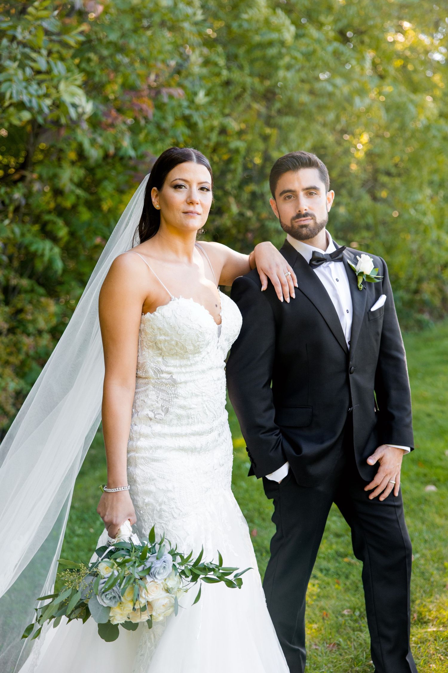 An outdoor wedding portrait featuring a couple in classic formal attire with a natural backdrop.