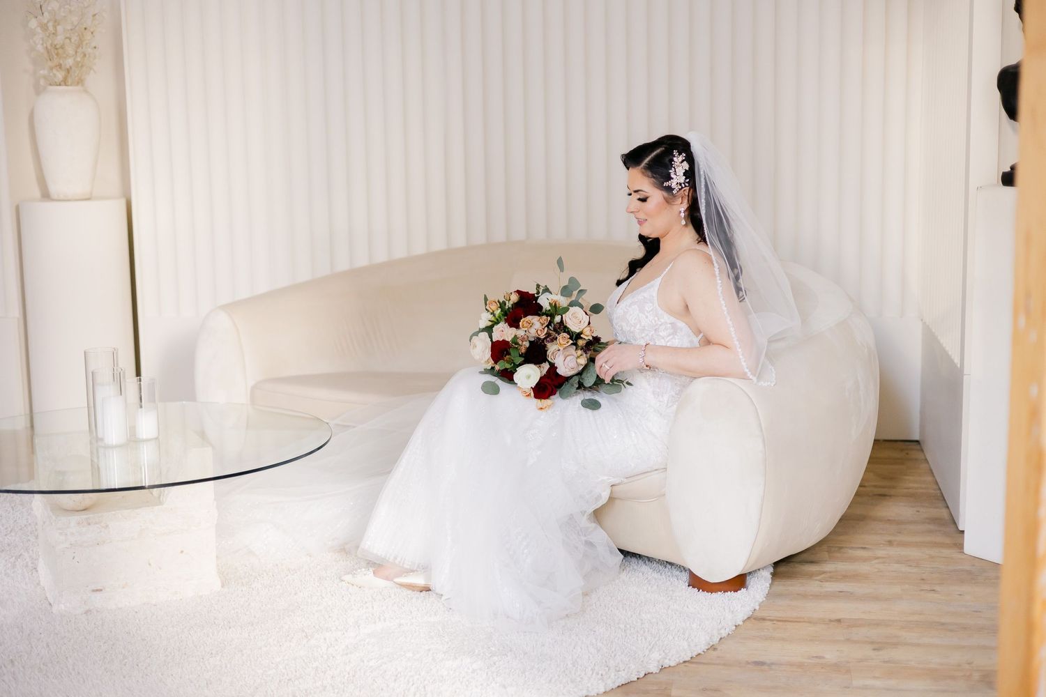 Bride seated on white chair holding romantic burgundy and blush bouquet.