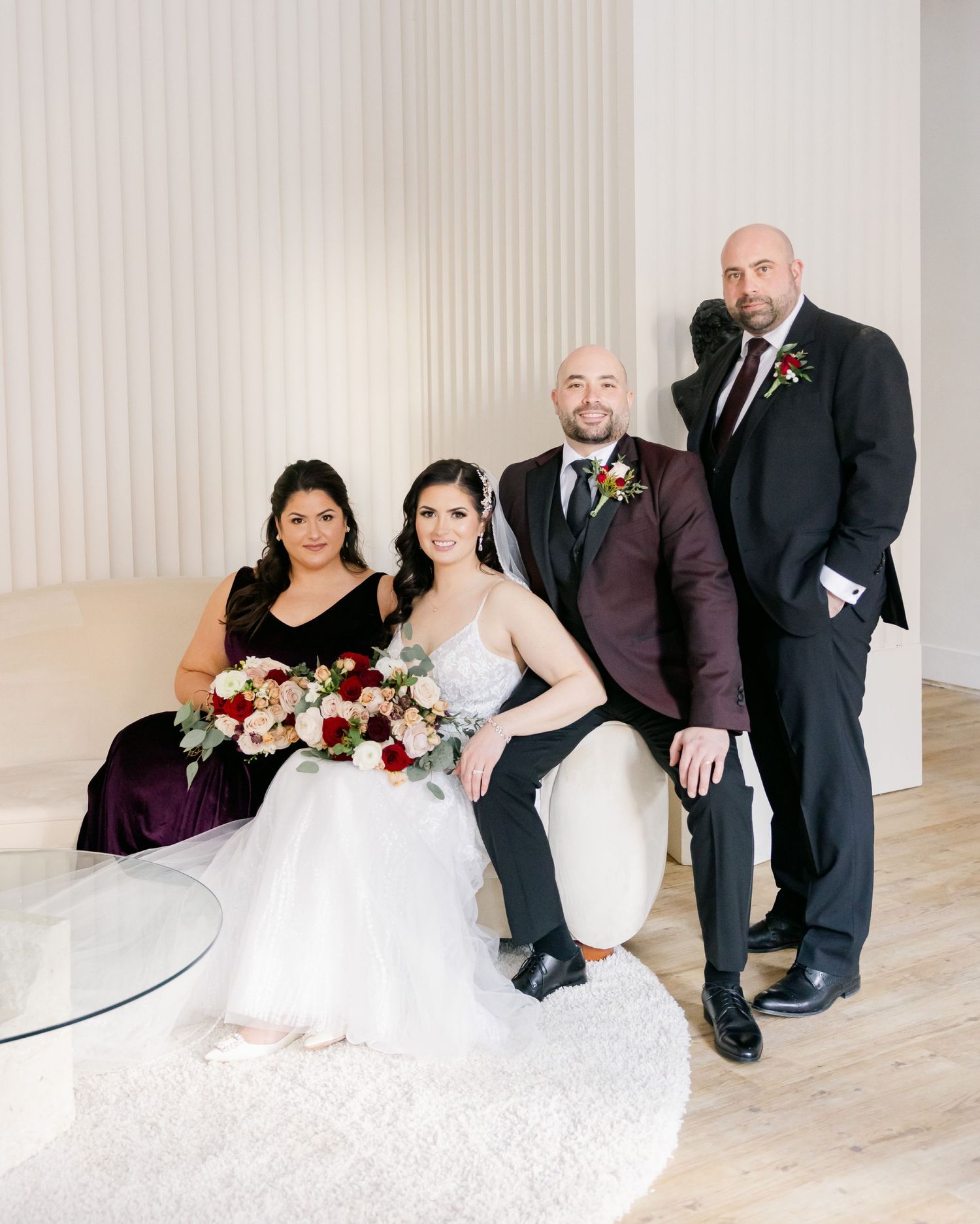 Wedding party group photo with burgundy accents against white modern backdrop.