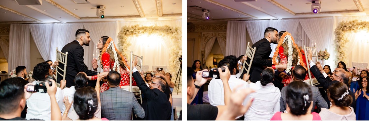 Wedding celebration with guests lifting the couple on chairs during traditional reception festivities.