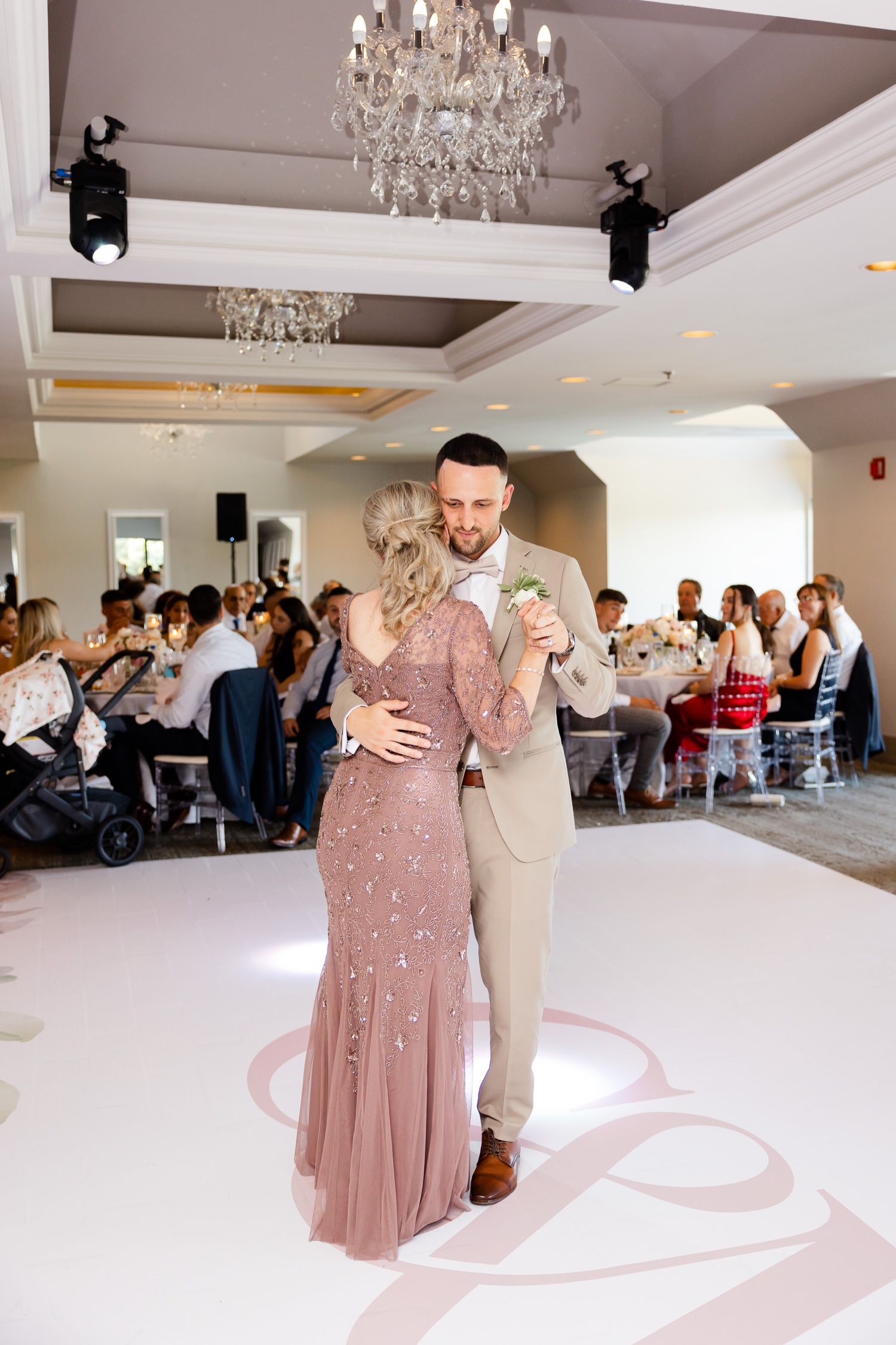Couple dancing in the spotlight at an elegant ballroom reception with crystal chandeliers overhead.