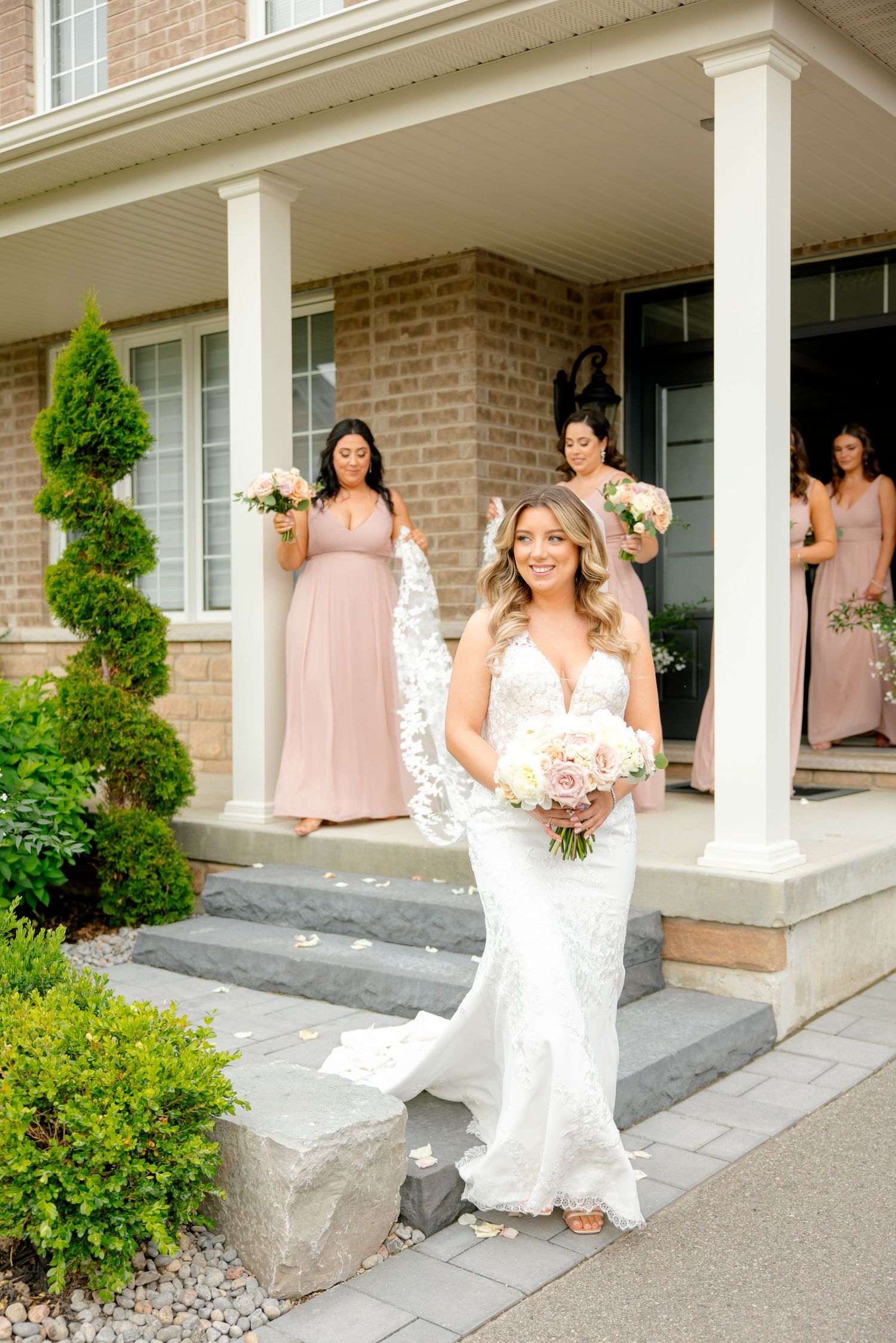 Wedding party in blush gowns posing on modern porch with brick and white columns.
