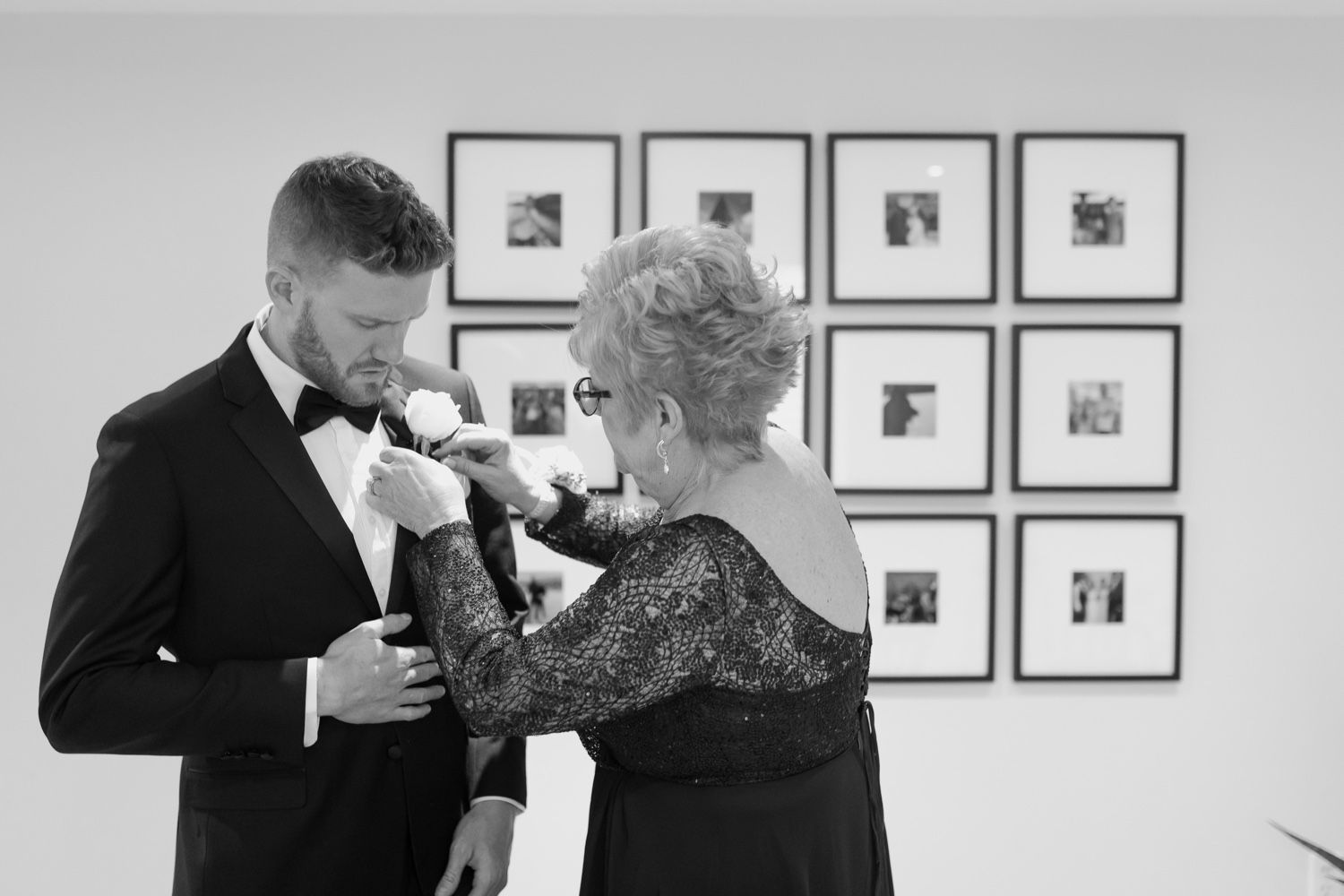 Black and white photo of formal moment between two people with framed photos in background.