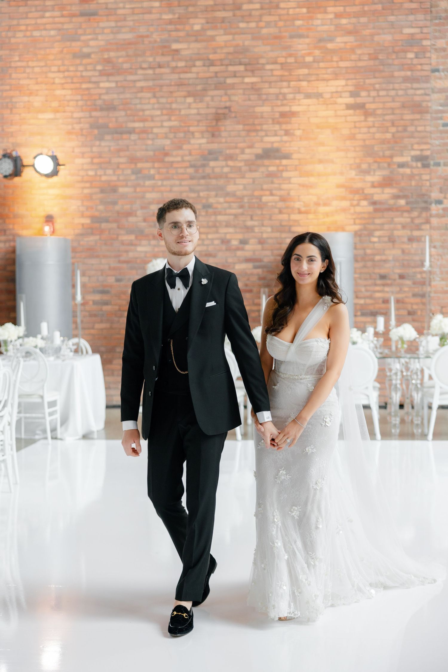 Couple posing in formal attire against a brick wall in an elegant reception venue.
