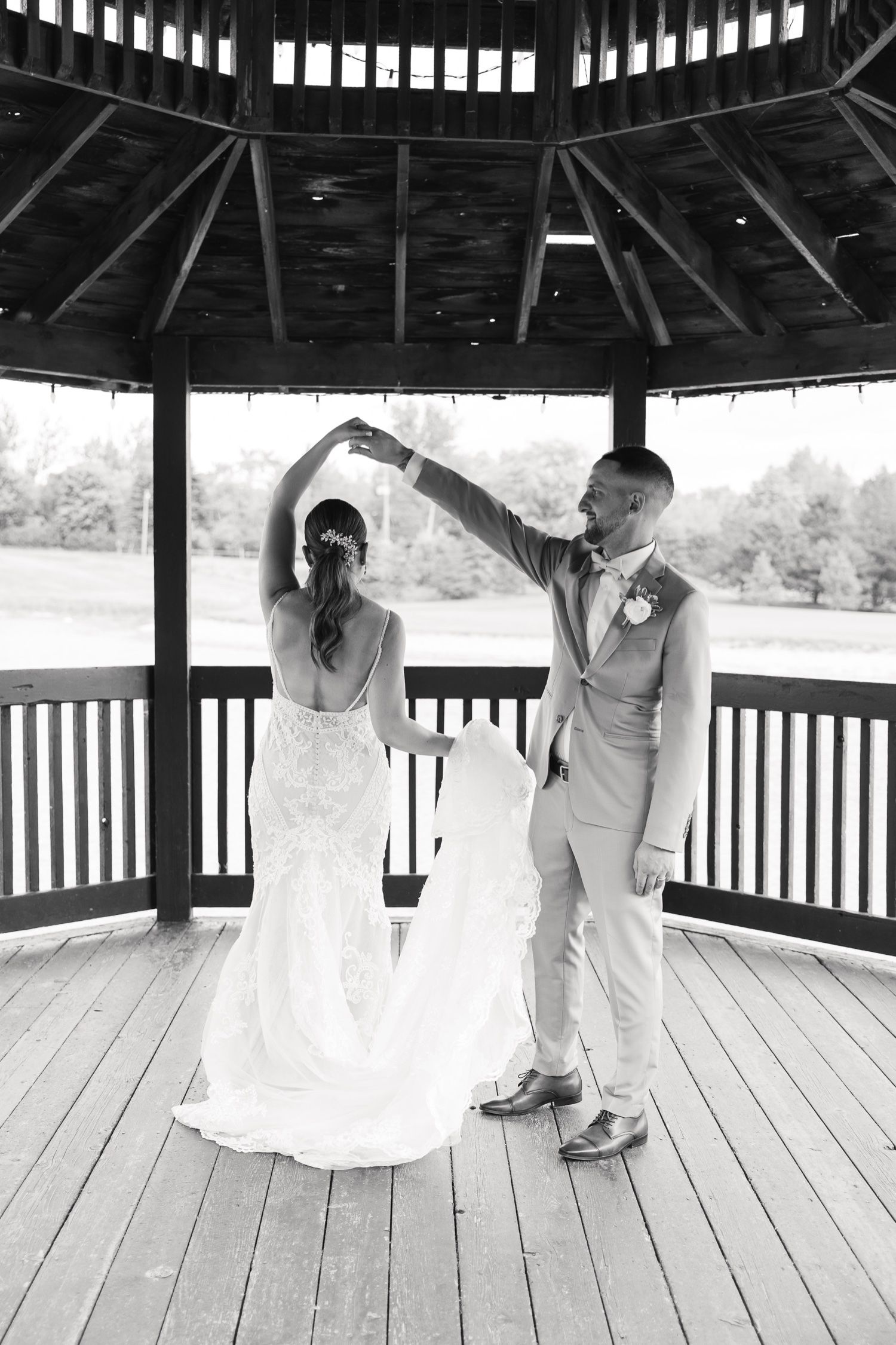 A black and white photo captures a dancing couple in a gazebo with decorative wooden beams overhead.