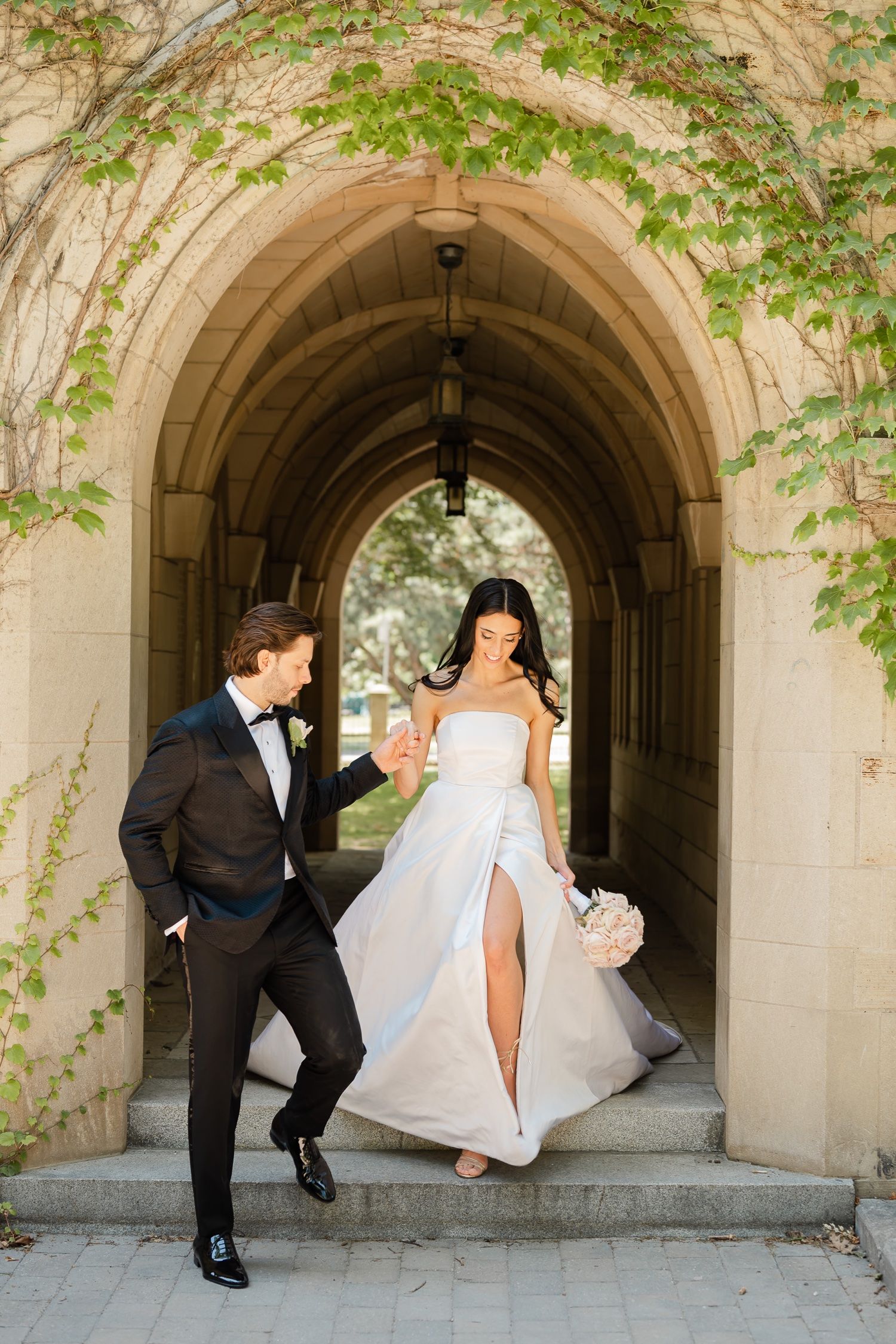A couple poses elegantly in a stone archway covered with green vines.