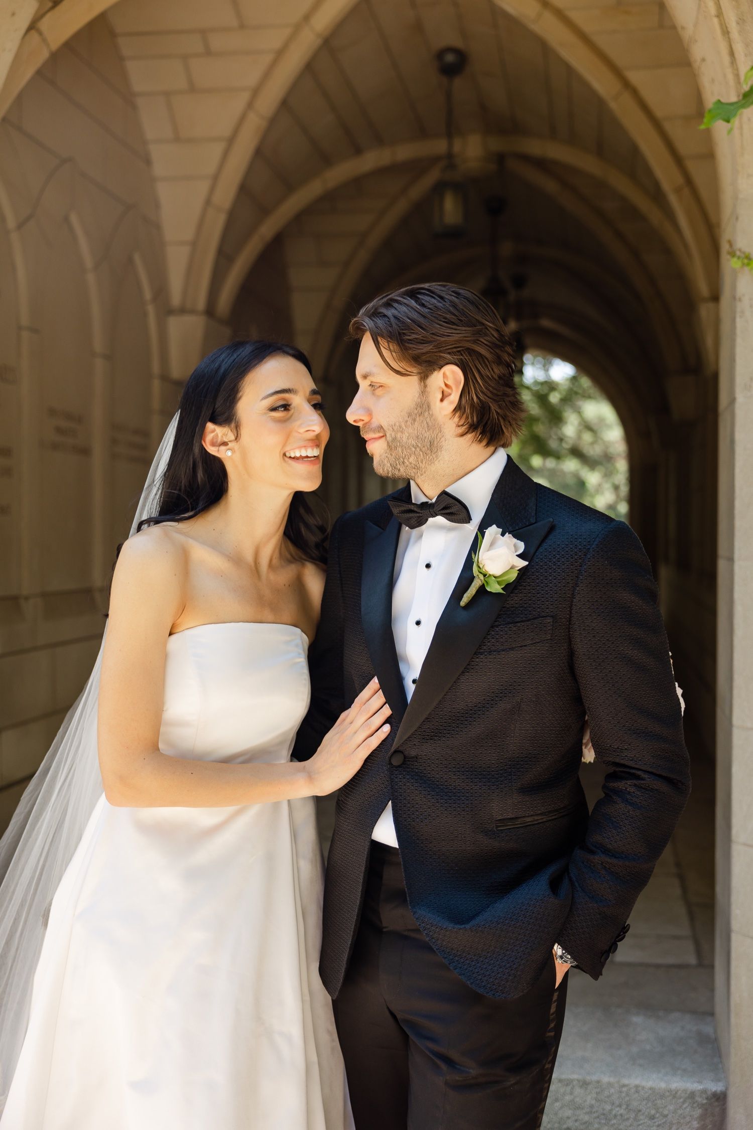 Romantic wedding moment captured in ornate stone corridor with vaulted ceiling.
