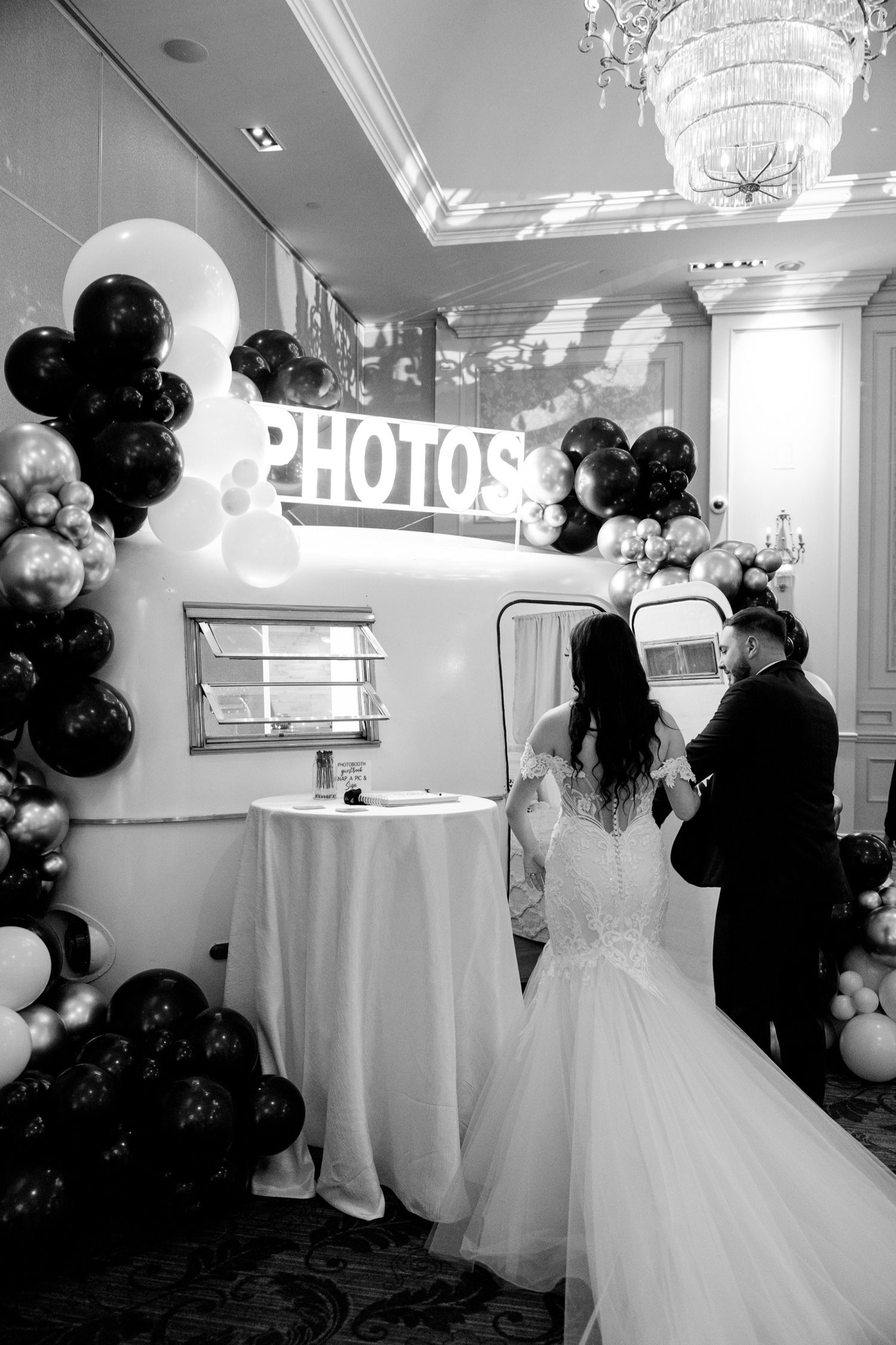 Wedding photo booth setup with black and white balloon arch and illuminated PHOTOS sign.