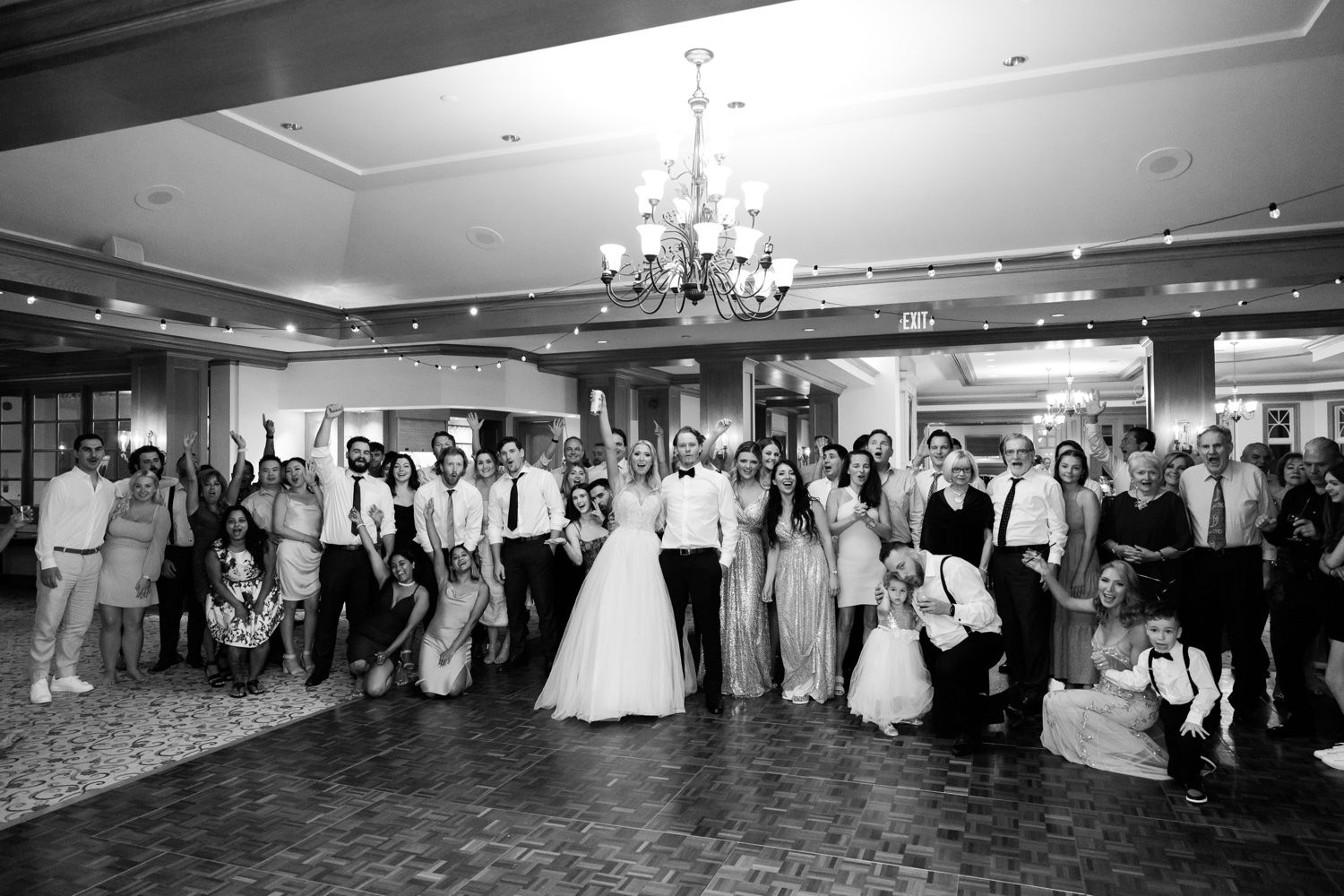 Black and white photo of wedding reception guests gathered on a grand ballroom dance floor.