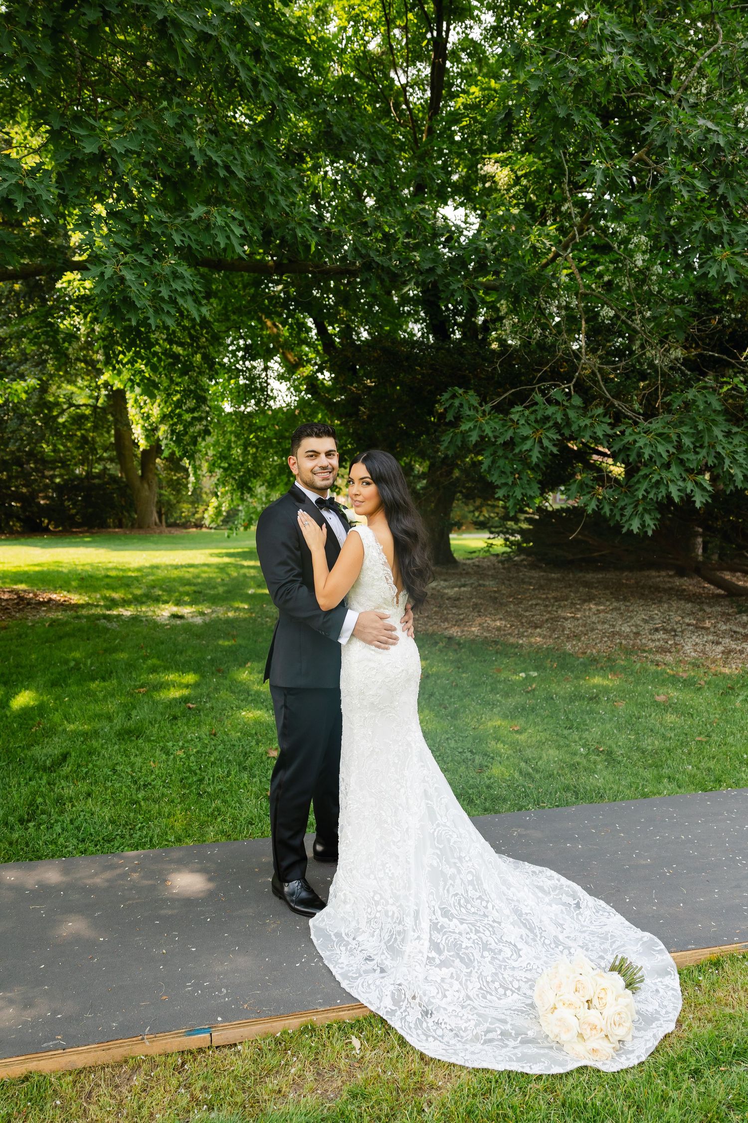 A beautiful wedding photo of a couple posing on a pathway with a bouquet of roses.