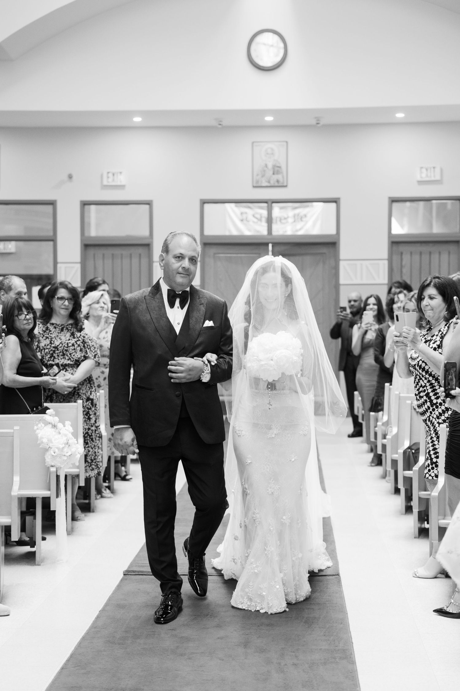 Black and white photo of a bride walking down the church aisle with her father during a traditional ceremony.
