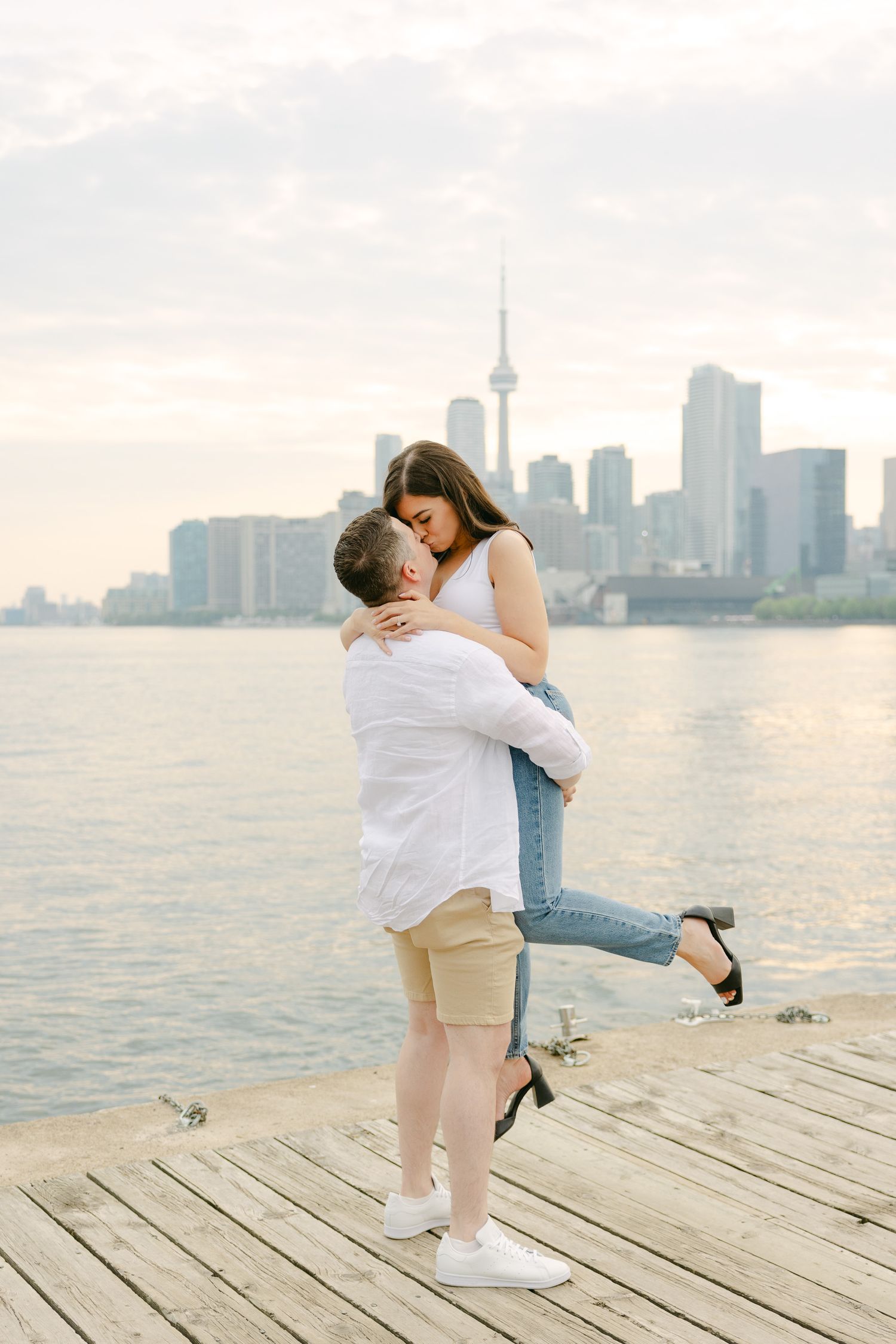 A playful moment on a wooden pier with Toronto's iconic CN Tower visible in the background.