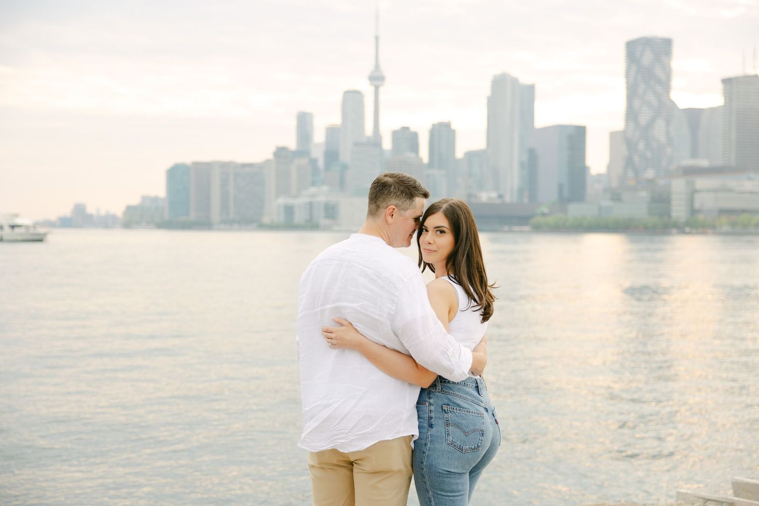 A couple shares an embrace by Lake Ontario with Toronto's urban skyline in the background.