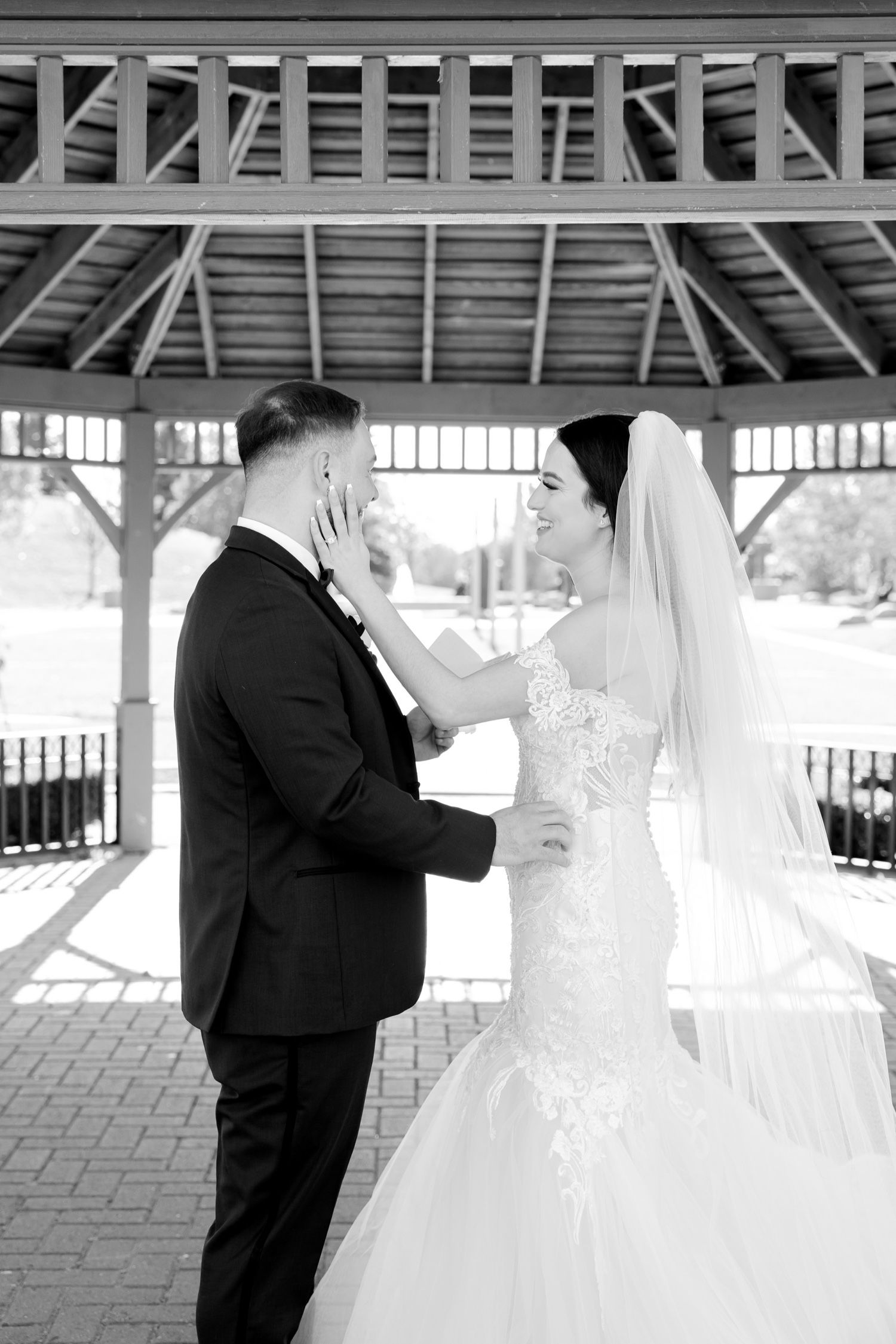 Black and white photo of a bride and groom sharing an intimate moment in a covered pavilion.