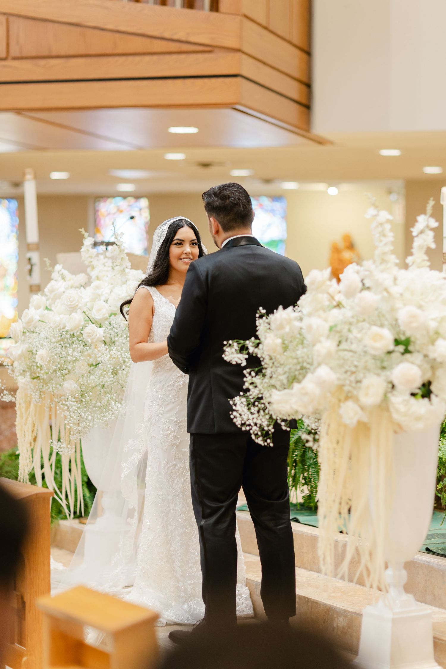 A wedding ceremony with a couple standing surrounded by white floral arrangements and decor in an elegant indoor venue.