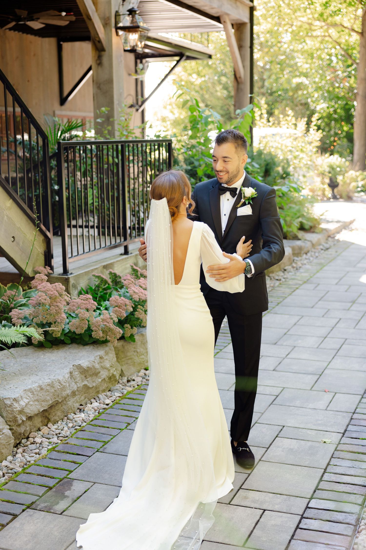 Couple shares an intimate moment on a stone walkway beneath wooden beams and garden foliage.