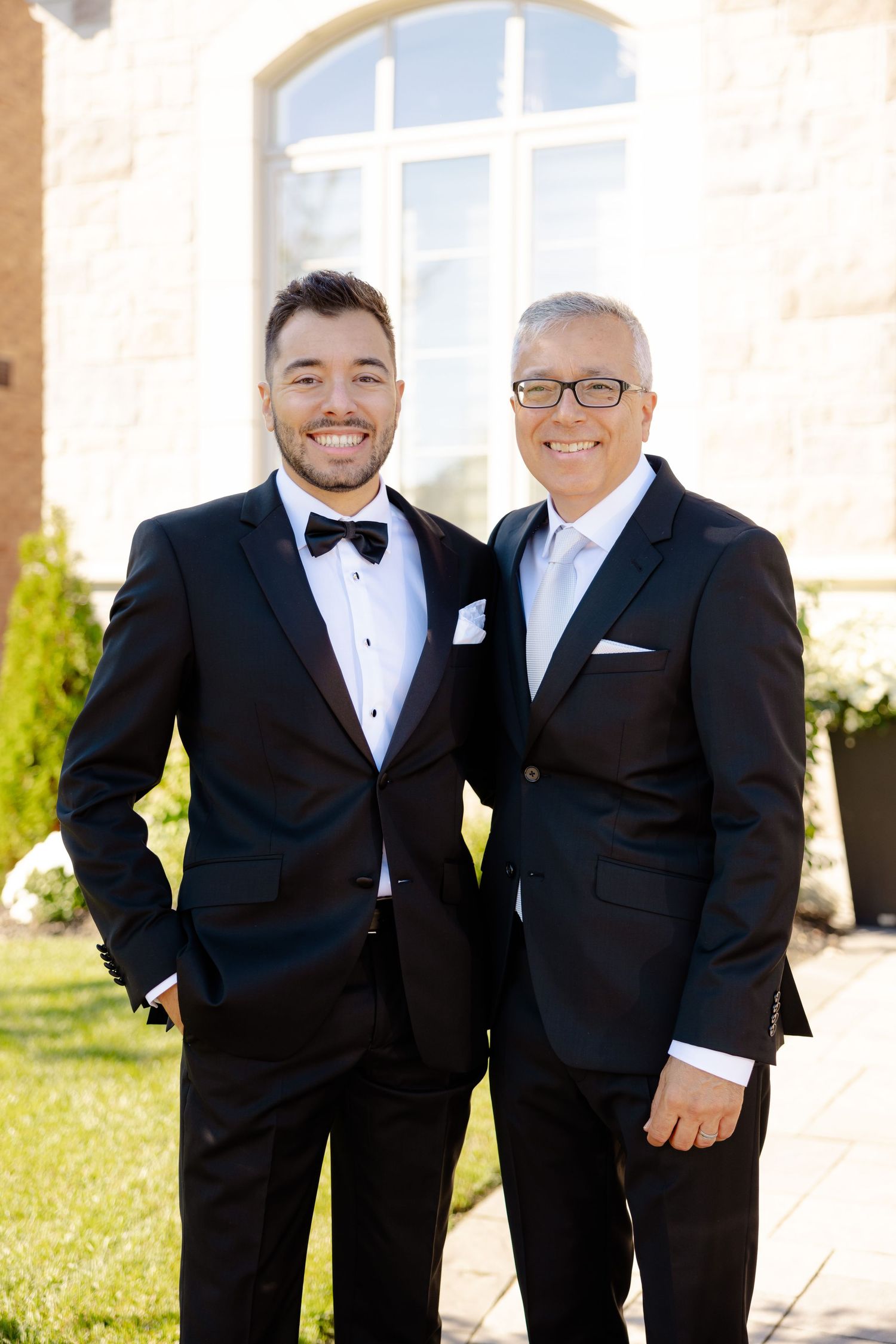 Wedding portrait of two people in formal attire standing in front of church window.