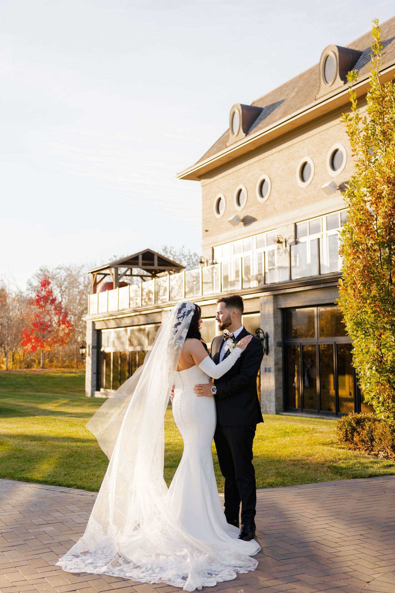 Romantic wedding portrait in front of elegant venue with autumn trees.