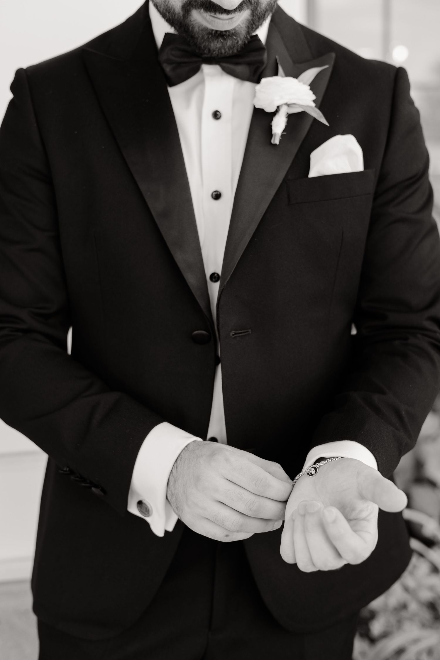Close-up detail of black tuxedo with white boutonniere and pocket square in classic monochrome style.
