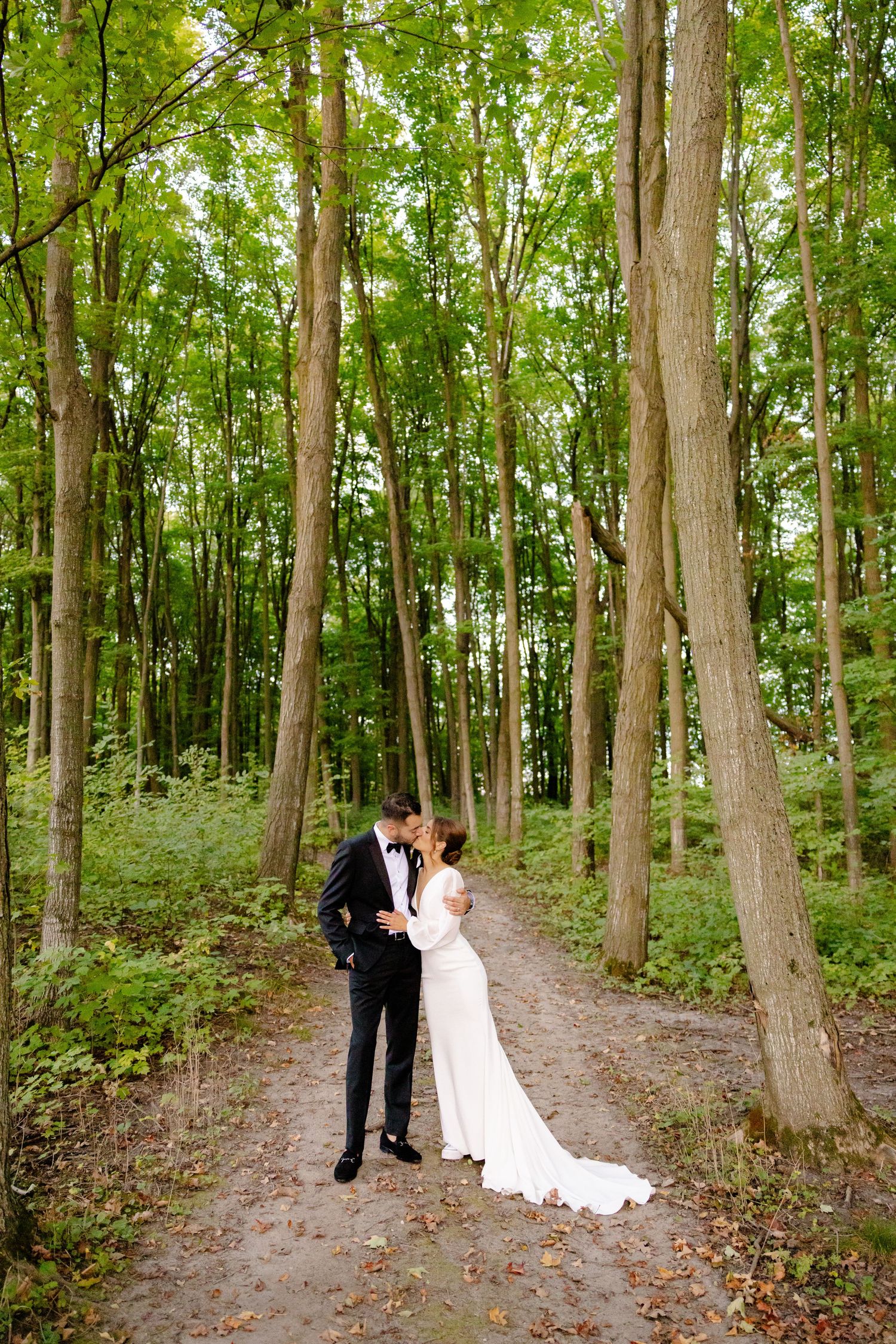 Romantic wedding portrait on a tree-lined path in a lush forest setting.