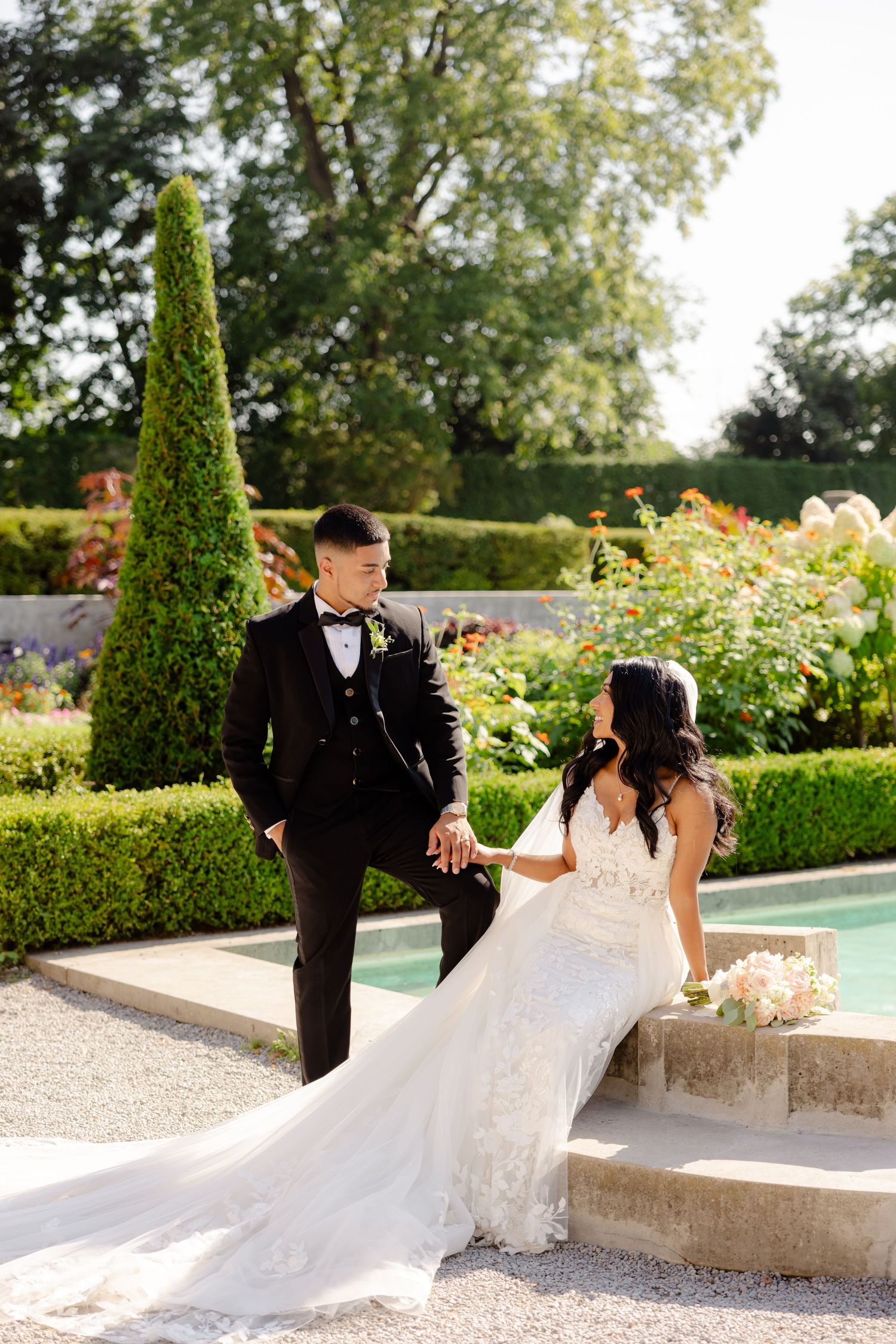 A couple shares a romantic moment on garden steps beside a reflecting pool and manicured landscaping.