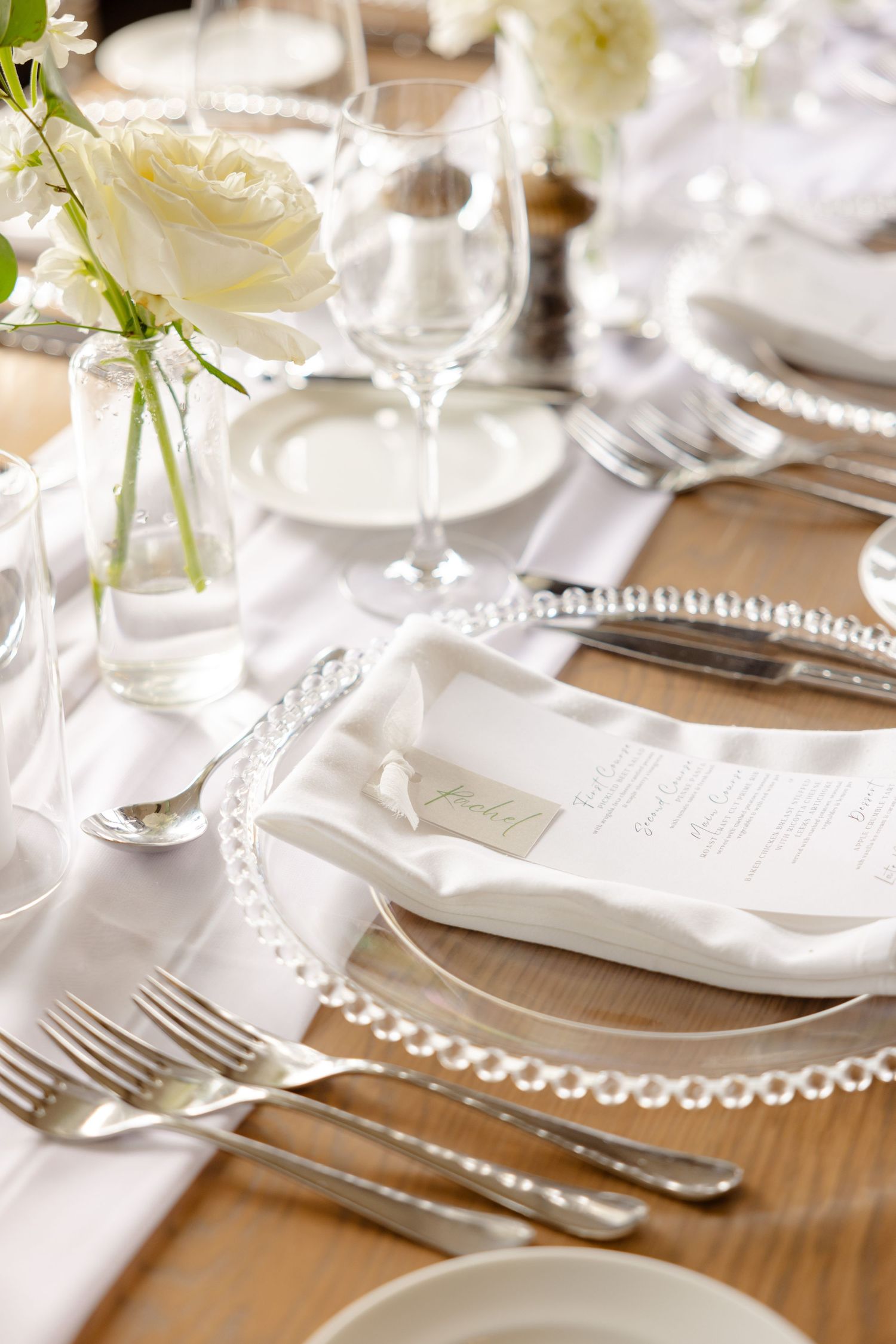 Detailed view of wedding place setting with pearl-edged charger plate and white menu card.