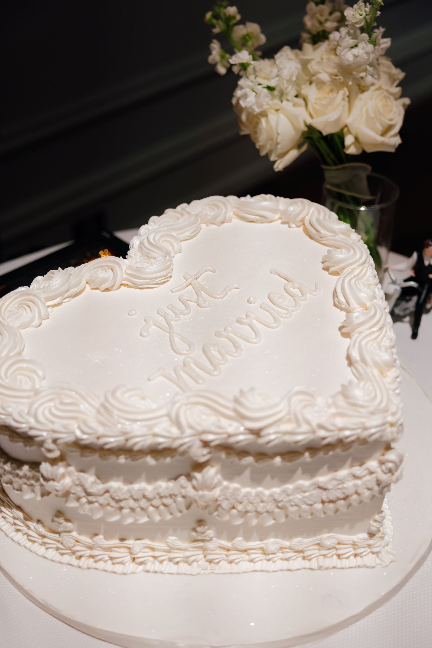 Detailed view of elegant heart-shaped wedding cake with white roses and delicate piping.