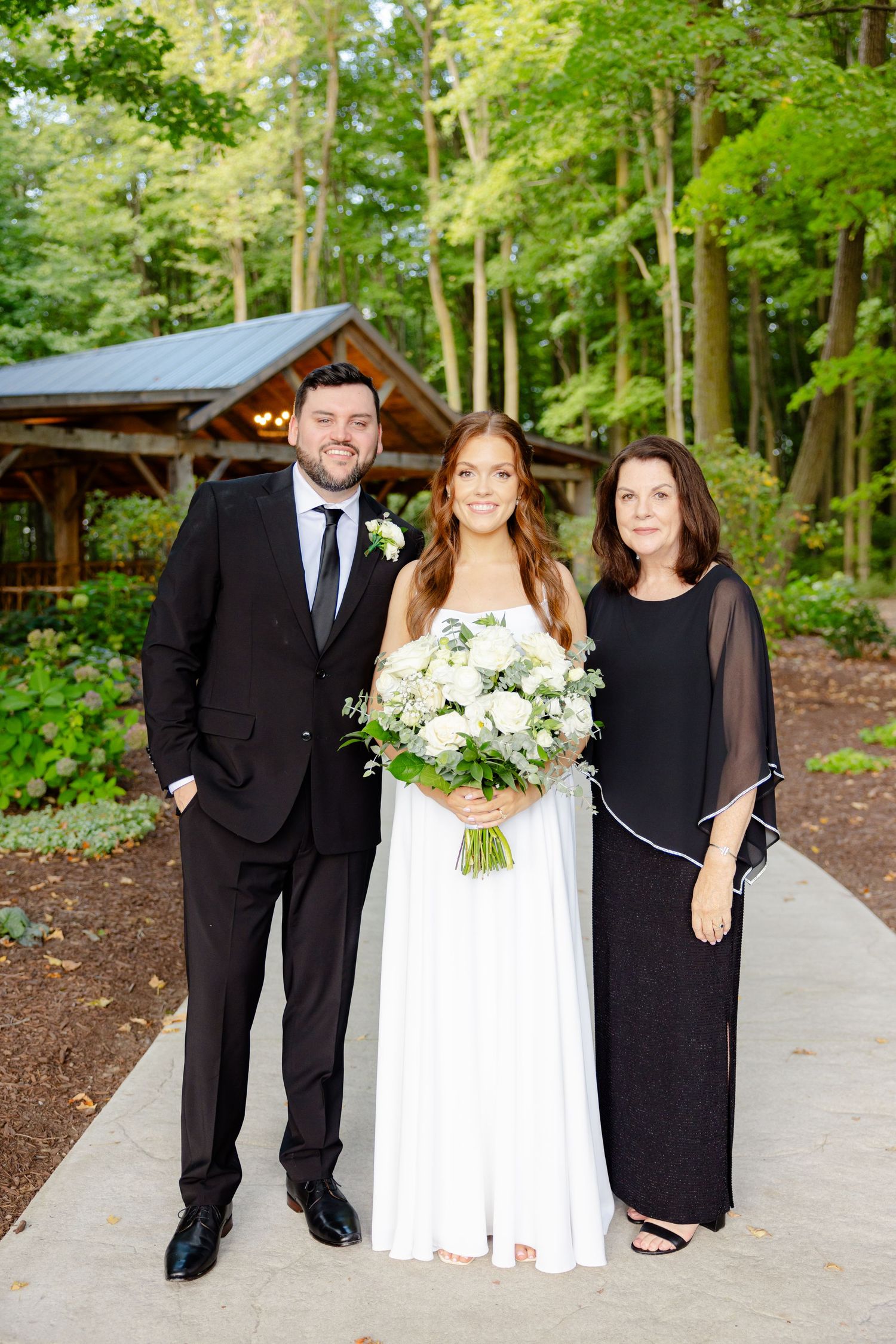 Wedding party portrait outside a rustic wooden pavilion surrounded by lush forest.