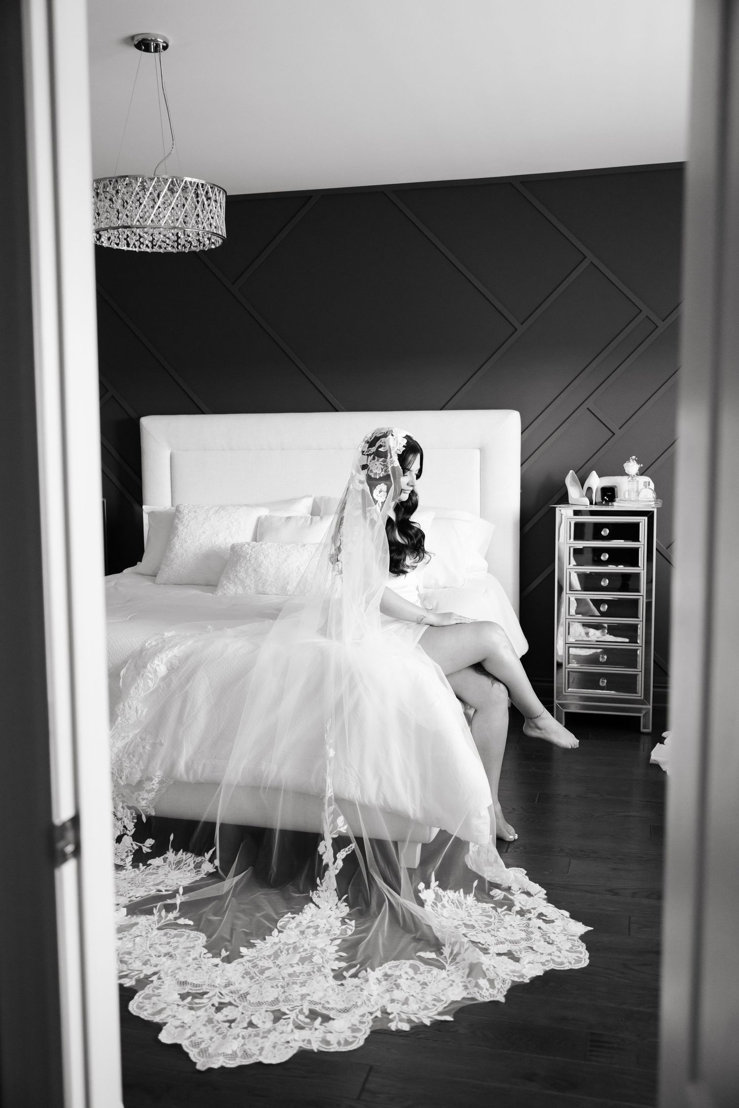 Black and white bridal portrait with intricate lace veil spread across bed.